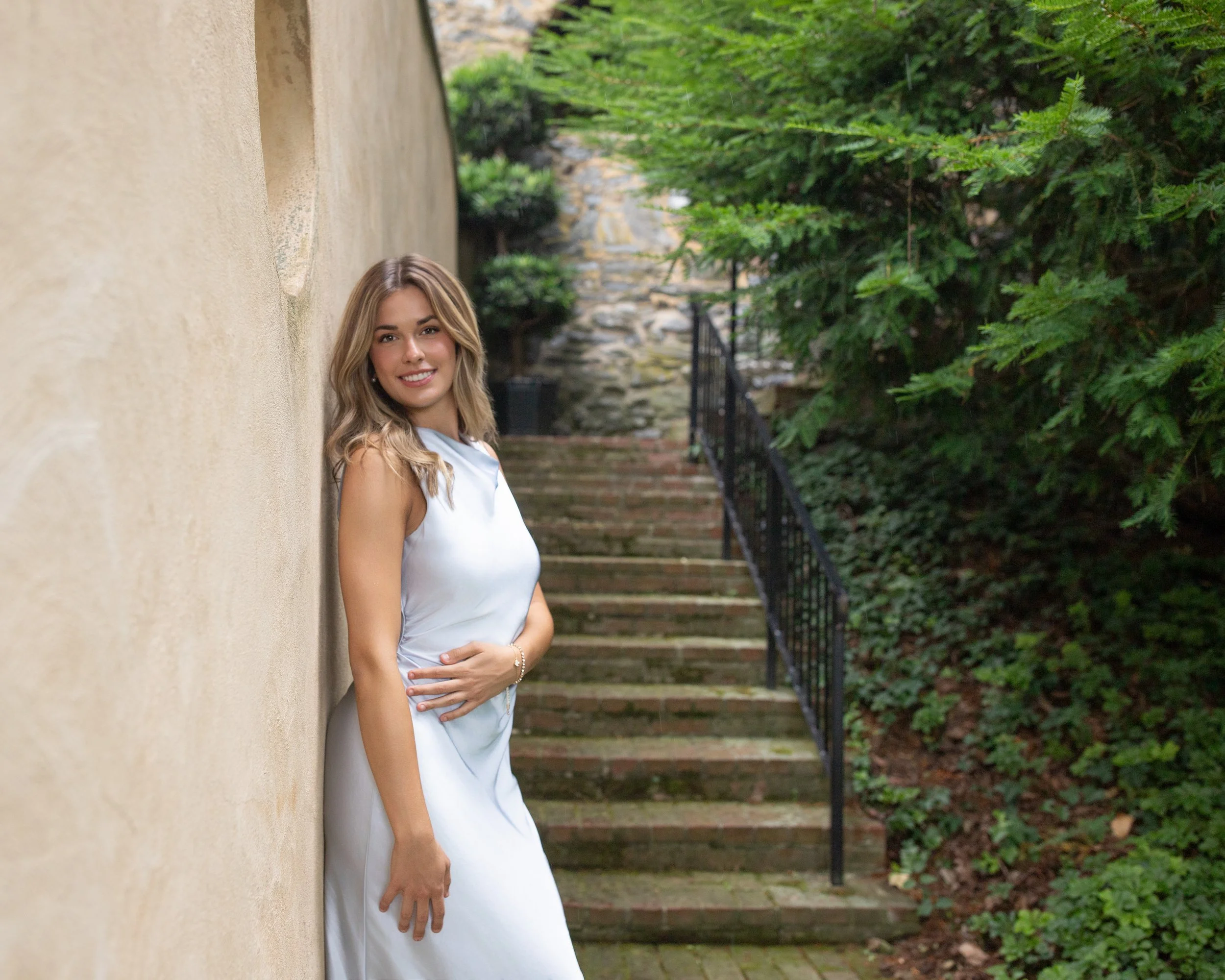 High school senior girl in a light blue dress posing beside a stone wall and garden steps during an outdoor senior portrait session in Lancaster, PA by Kat DiComo Photography.