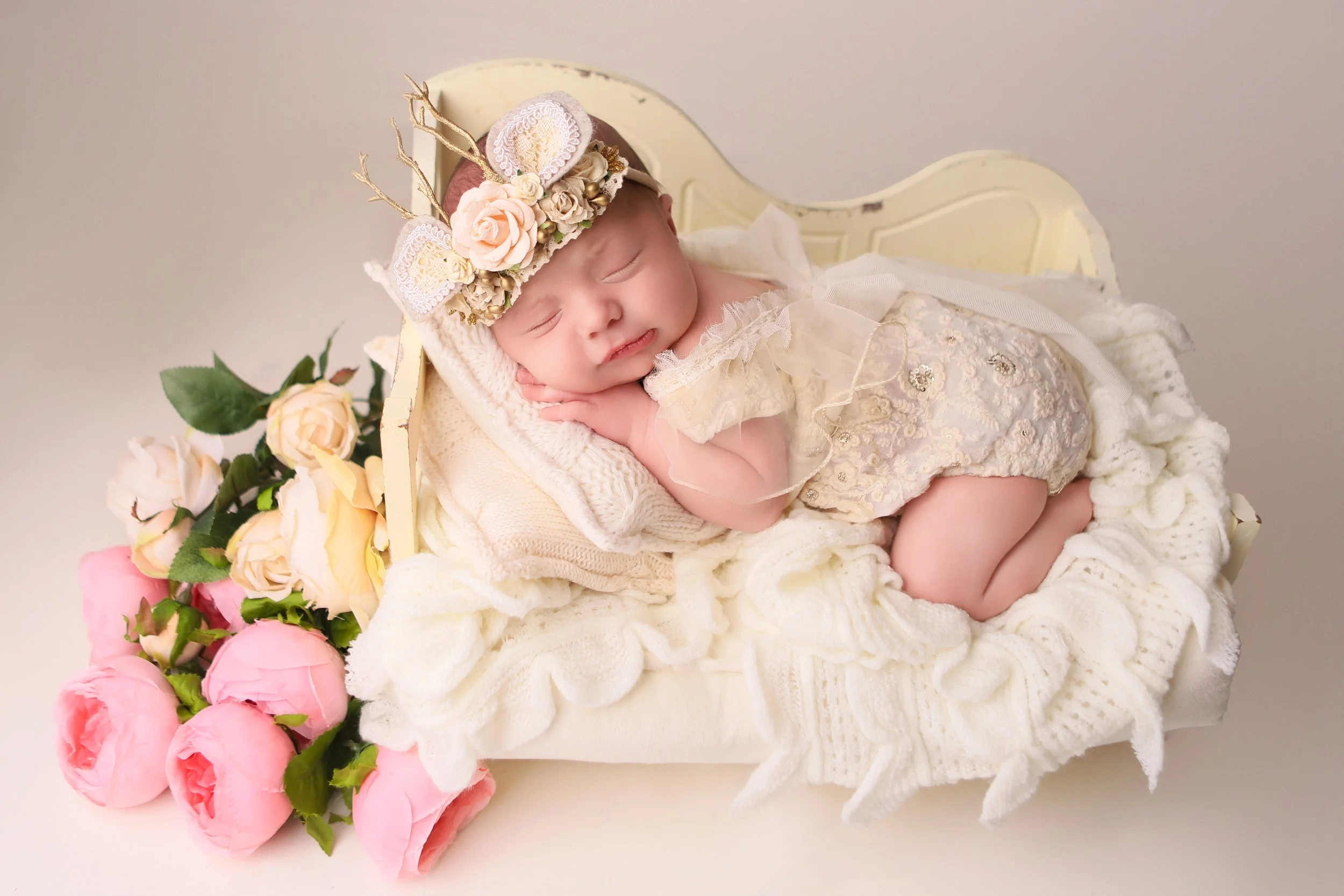 newborn baby girl laying in a bed with cream colored fabric with pink flowers