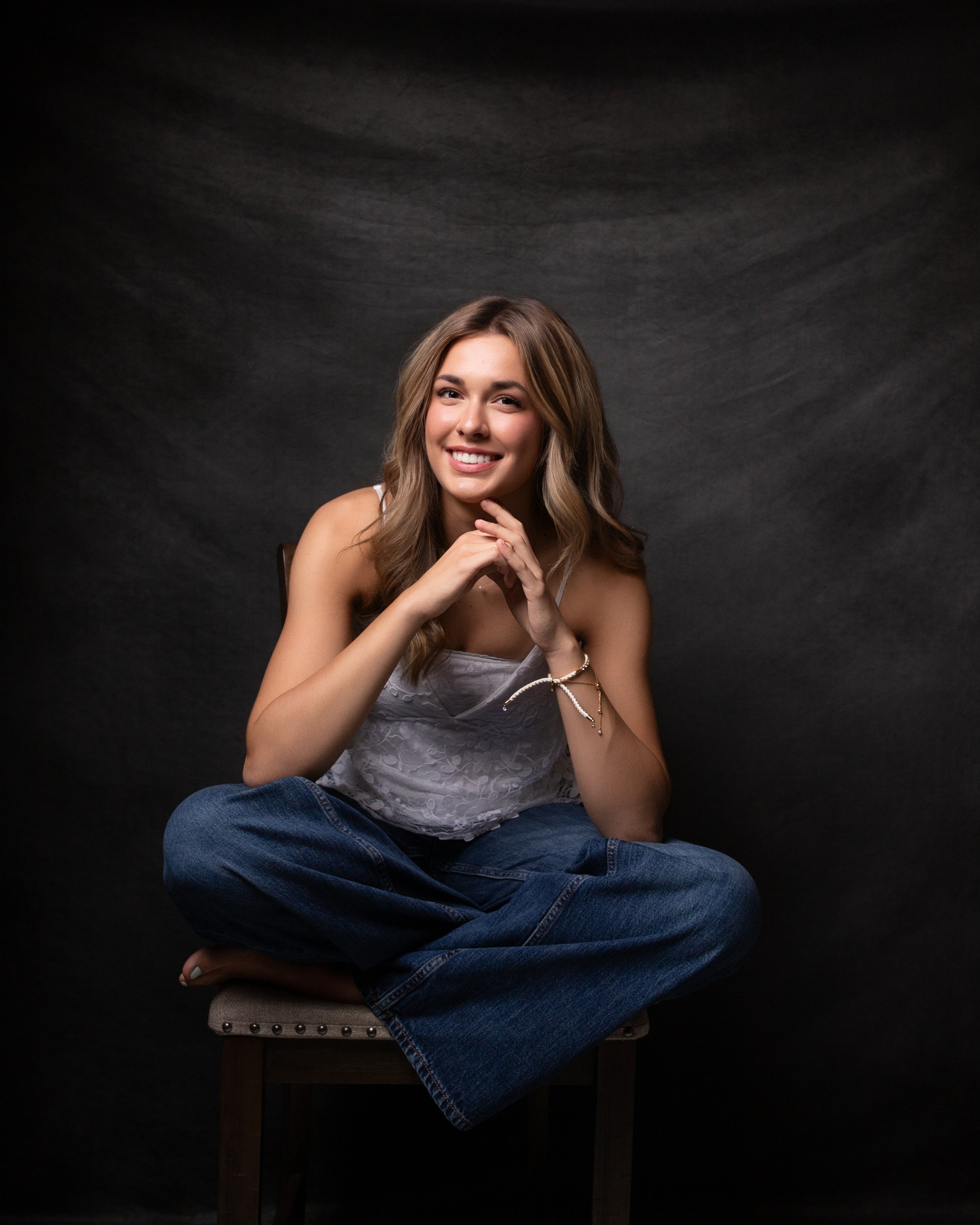 High school senior portrait of a smiling teenage girl in casual jeans and a white top photographed in a professional studio by Lancaster PA senior photographer Kat DiComo Photography.