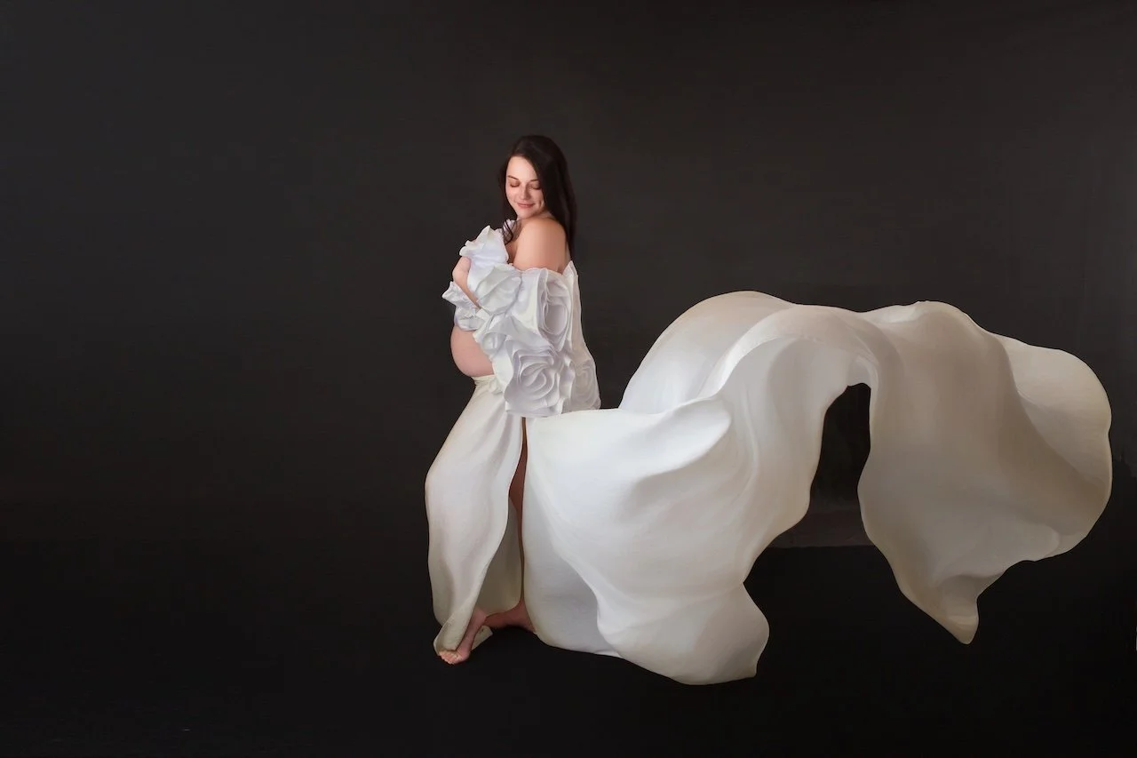 pregnant woman in a white floral dress with a white satin fabric train flowing