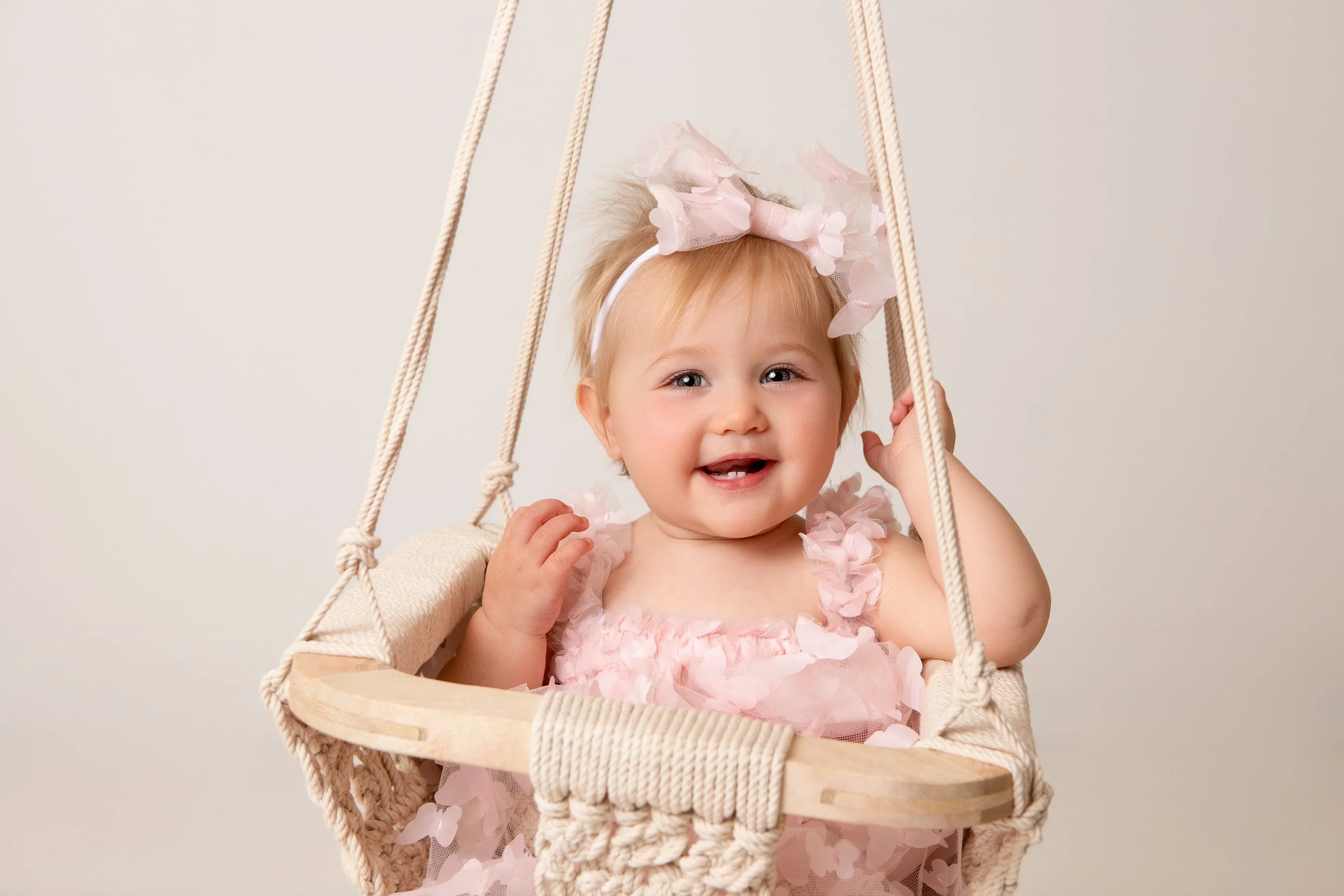 little girl smiling in a swing with a pink bow in her hair