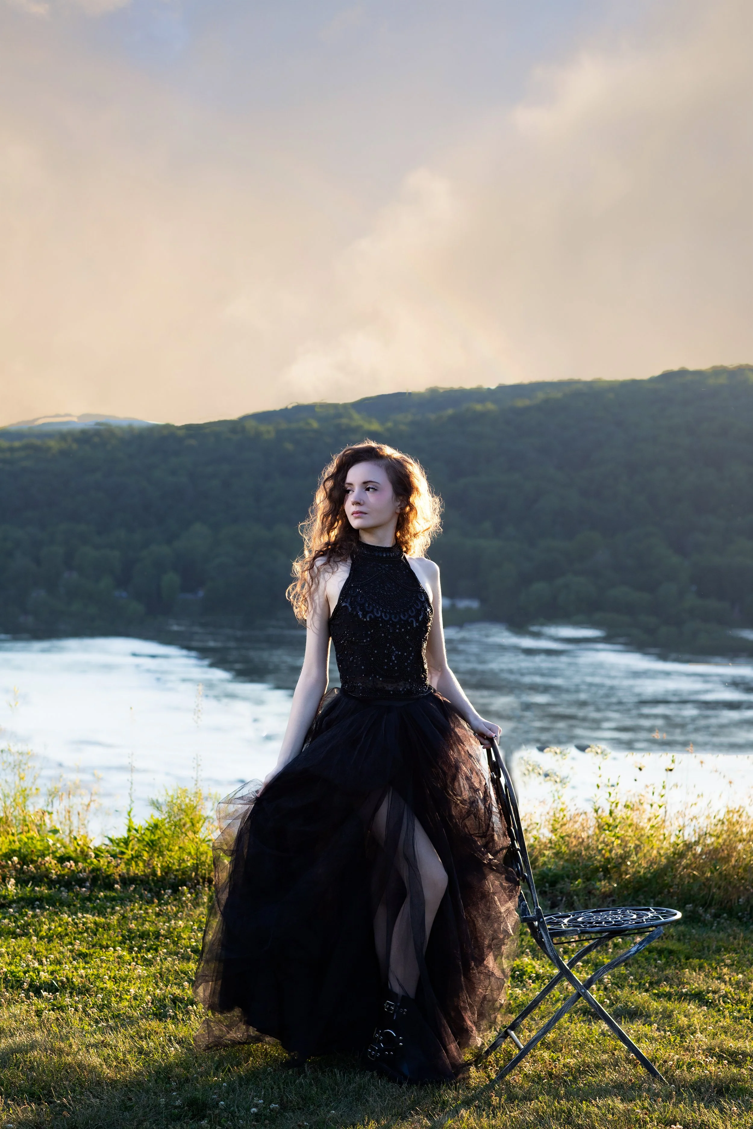 High school senior wearing an elegant black gown posing at sunset along the Susquehanna River in Lancaster, Pennsylvania. Golden backlighting highlights her hair, creating a timeless outdoor senior portrait with a scenic river backdrop.