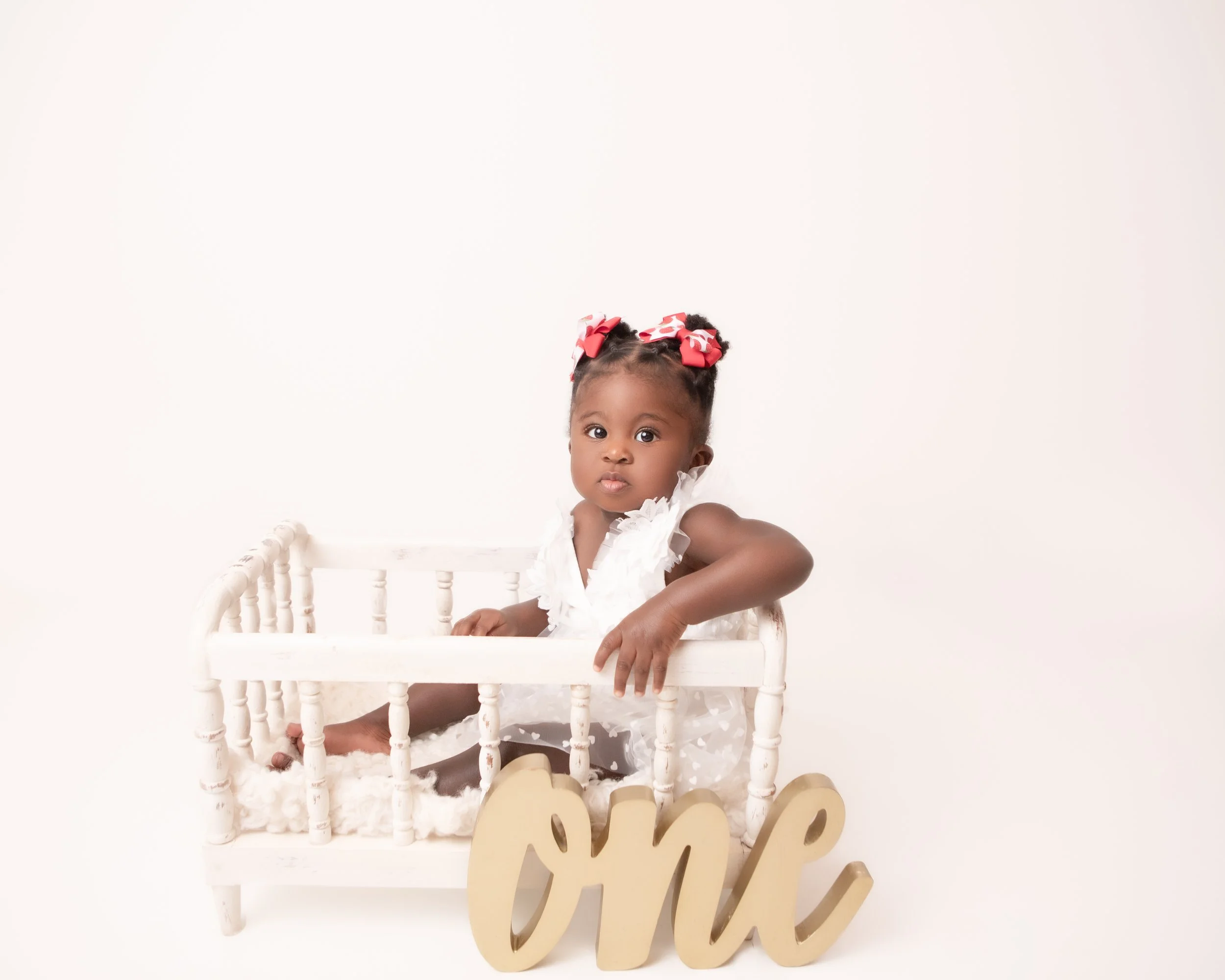little girl wearing a white dress sitting in a crib with the word one