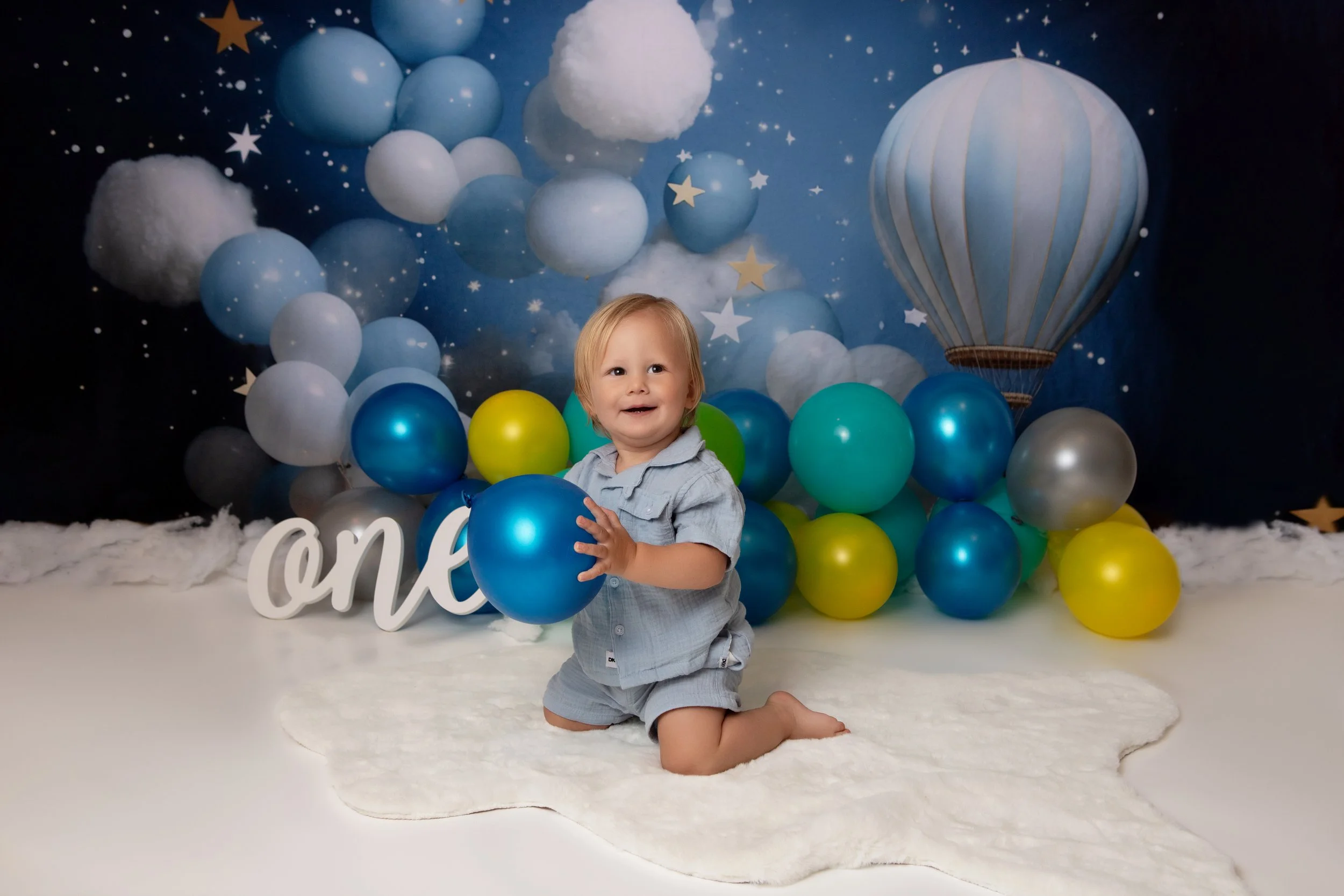 one year old boy sitting on his knees holidng a blue balloon