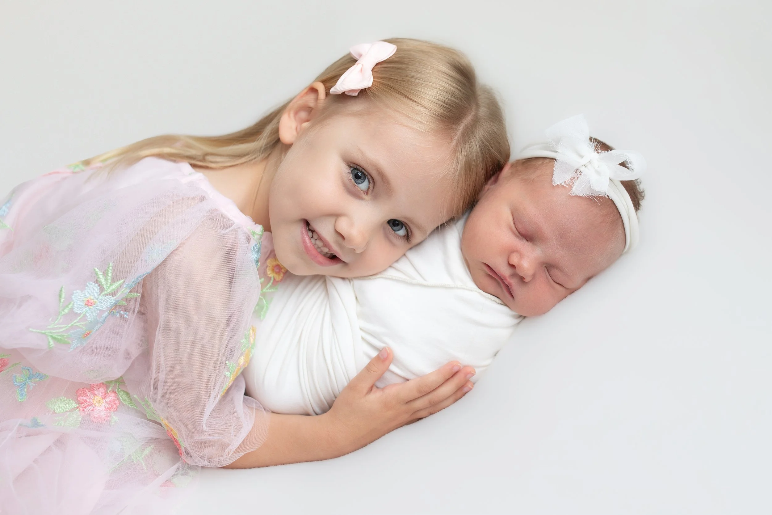 two children a toddler wearing a pink dress and newborn swaddled in white 