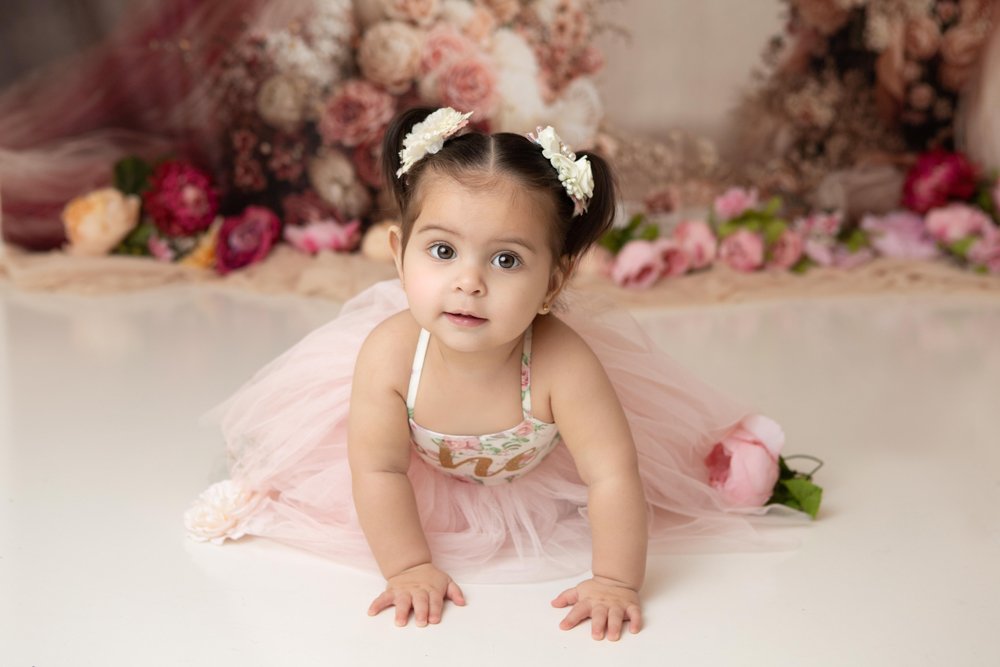 a one year old girl wearing a pink dres with floral background