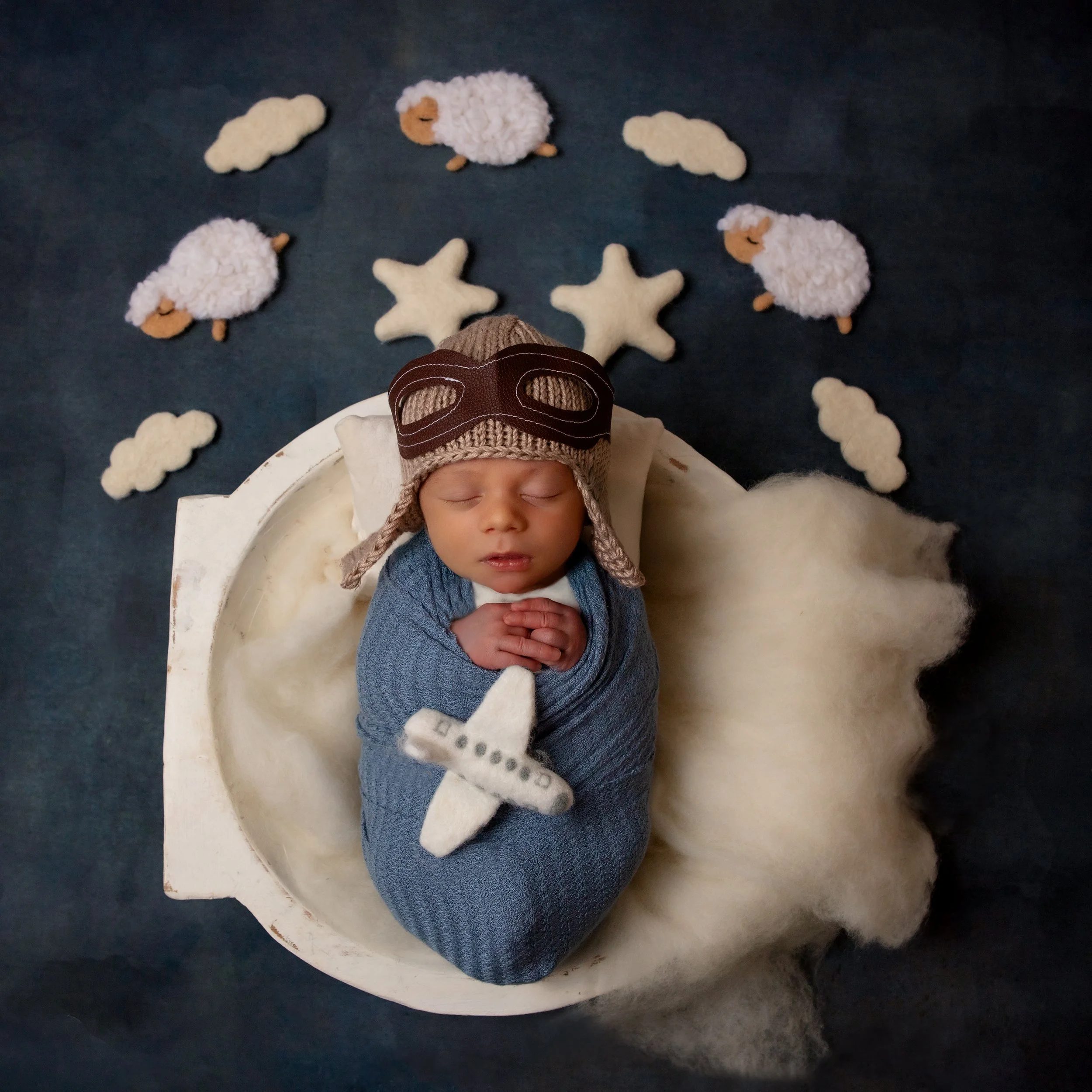 newborn baby boy with a pilot hat on holding an airplane with stars clouds and sheep