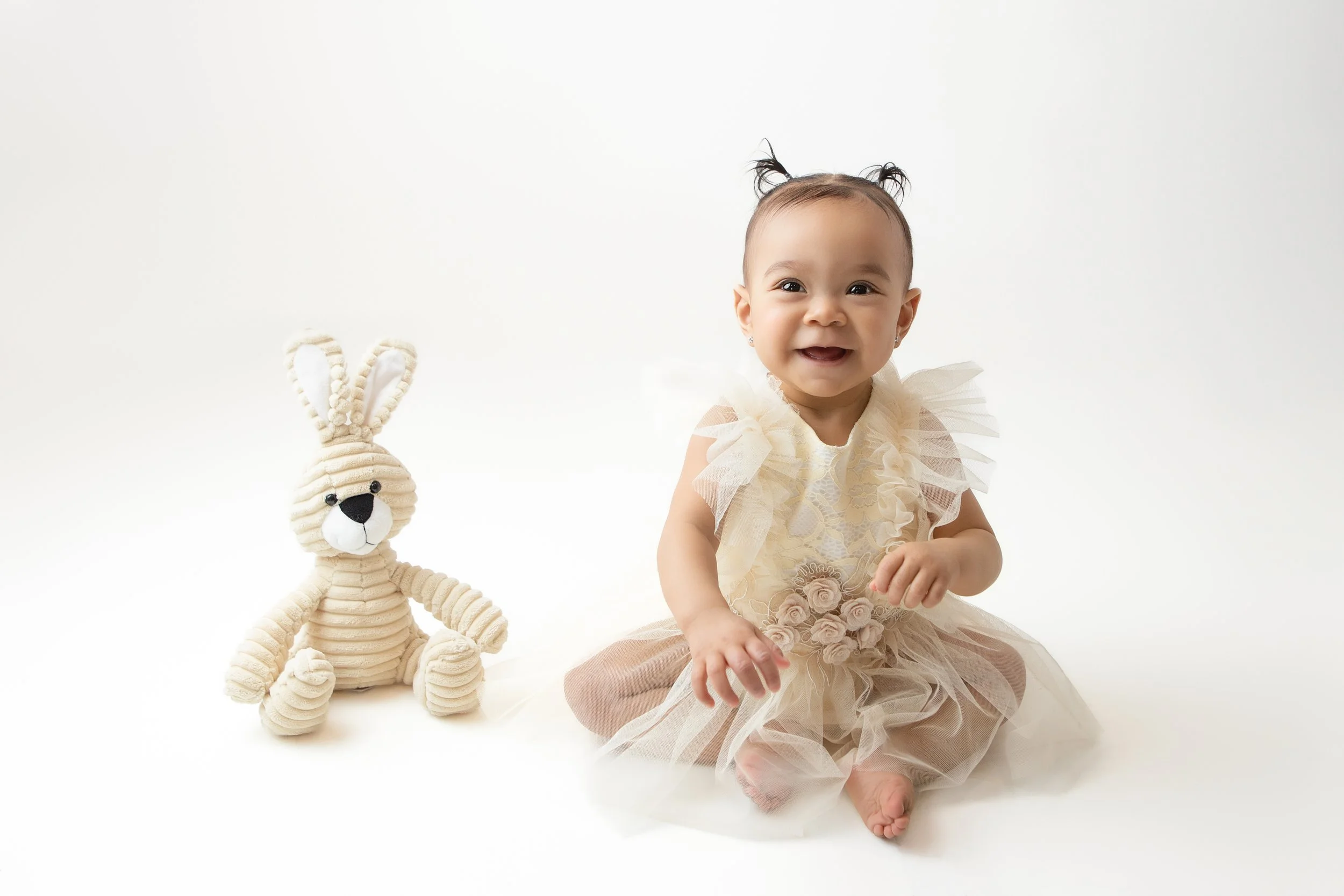 a smiling little girls with pig tails sitting next to a stuffed rabbit