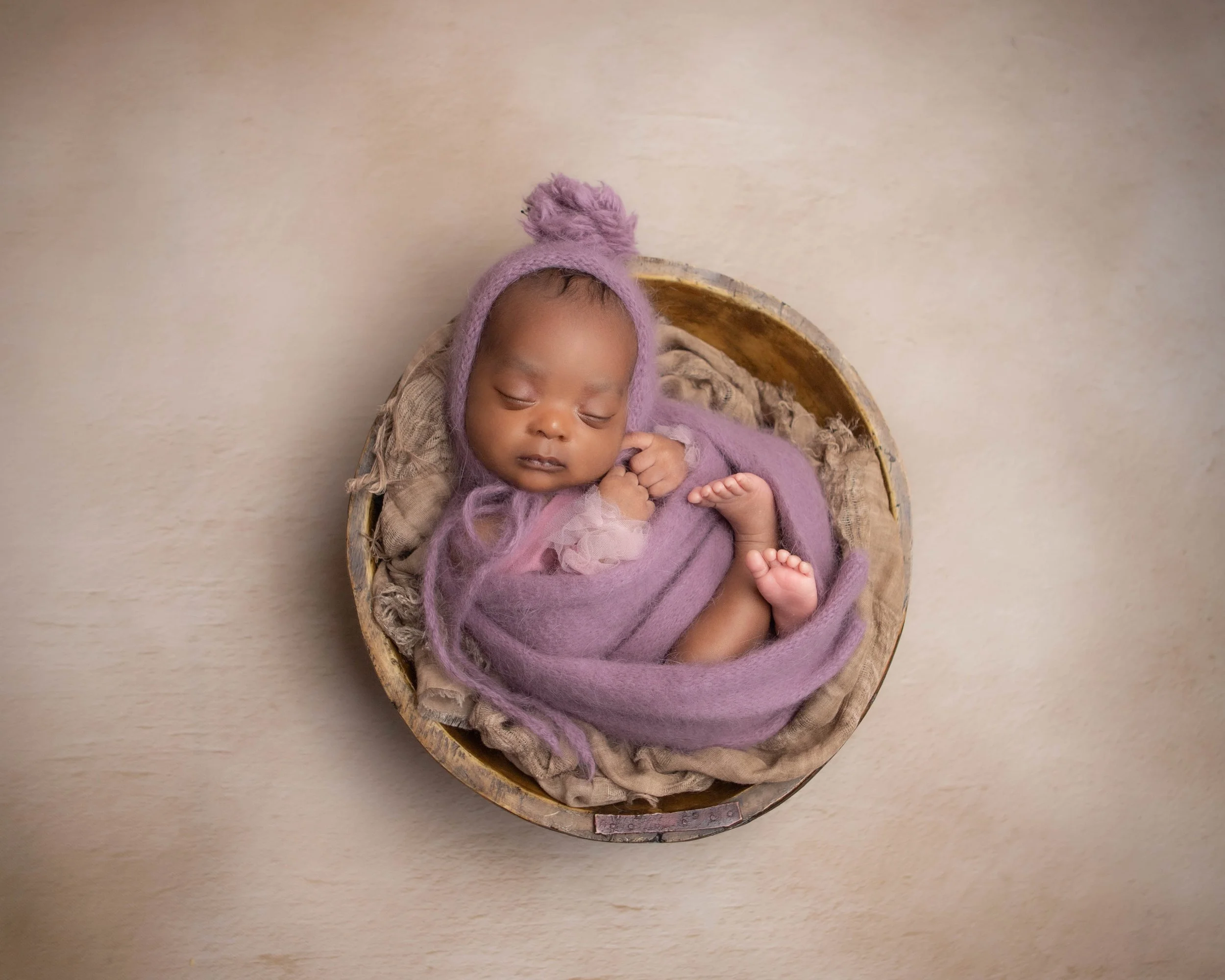 newborn baby girl wrapped in purple sleeping a bowl 