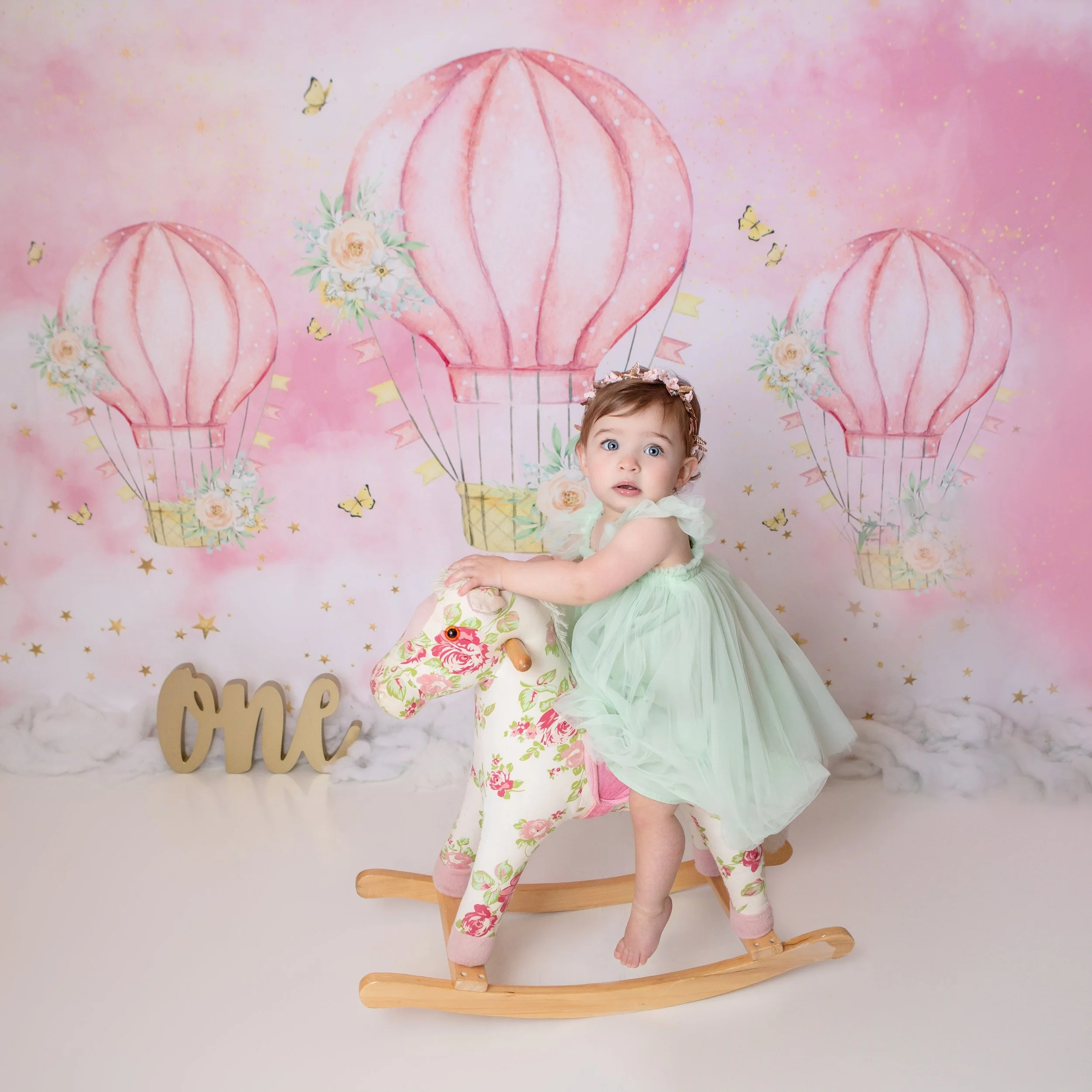 littel girl first birthday on a rocking horse with a pink hot air balloon background