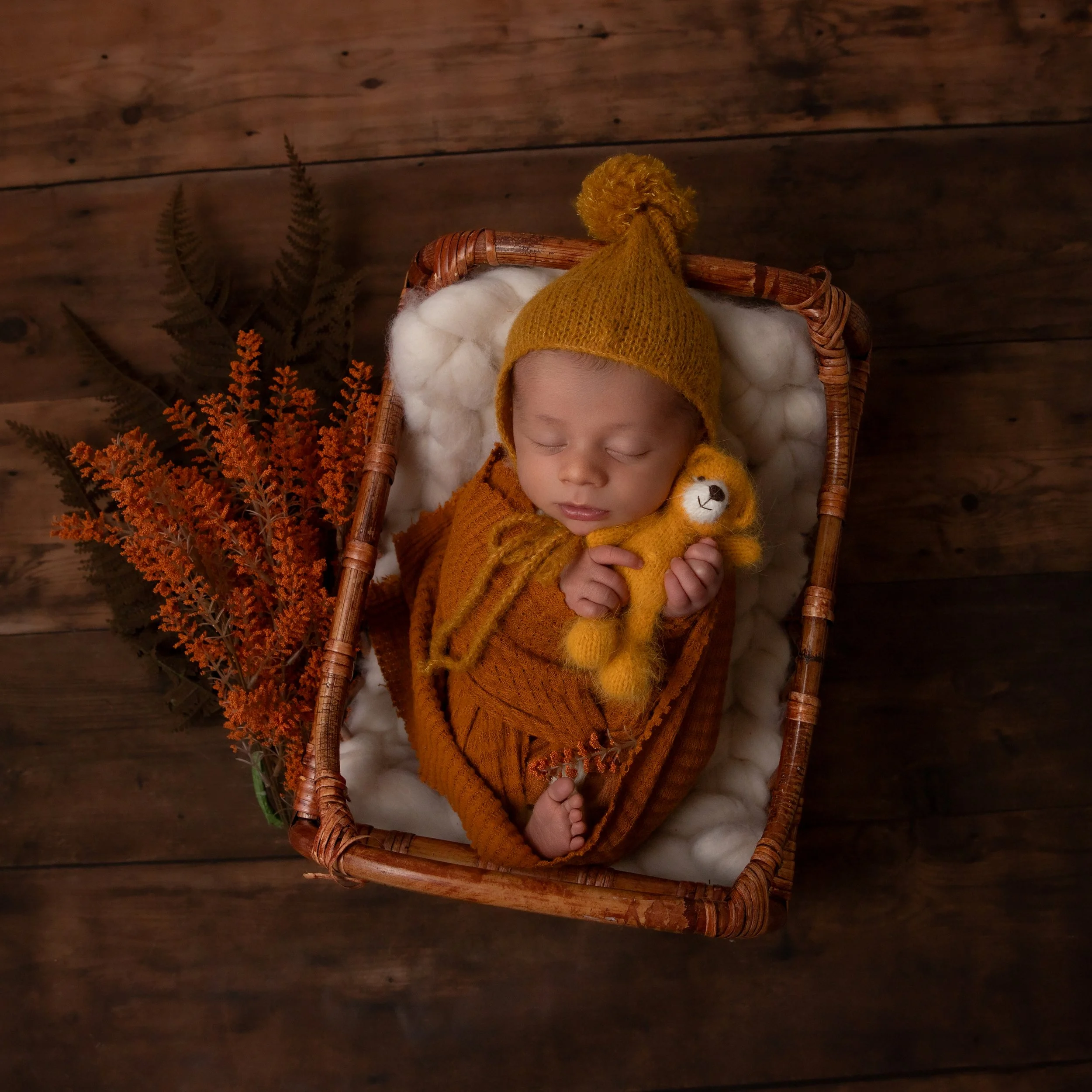 newborn baby boy in orange wrap holding an orange bear