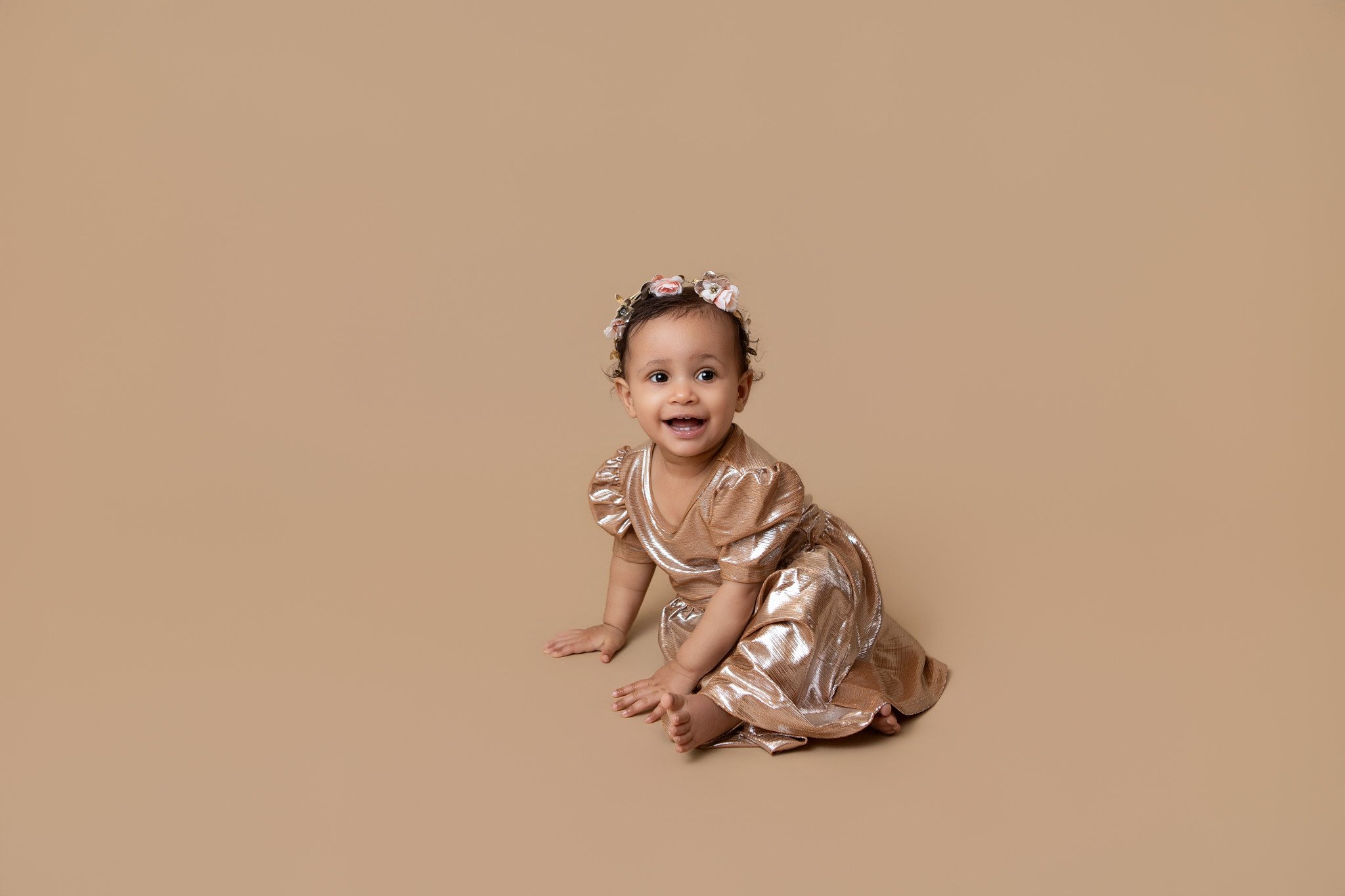 toddler girl wearing a shiny gold dress with a floral gold headband smiling 