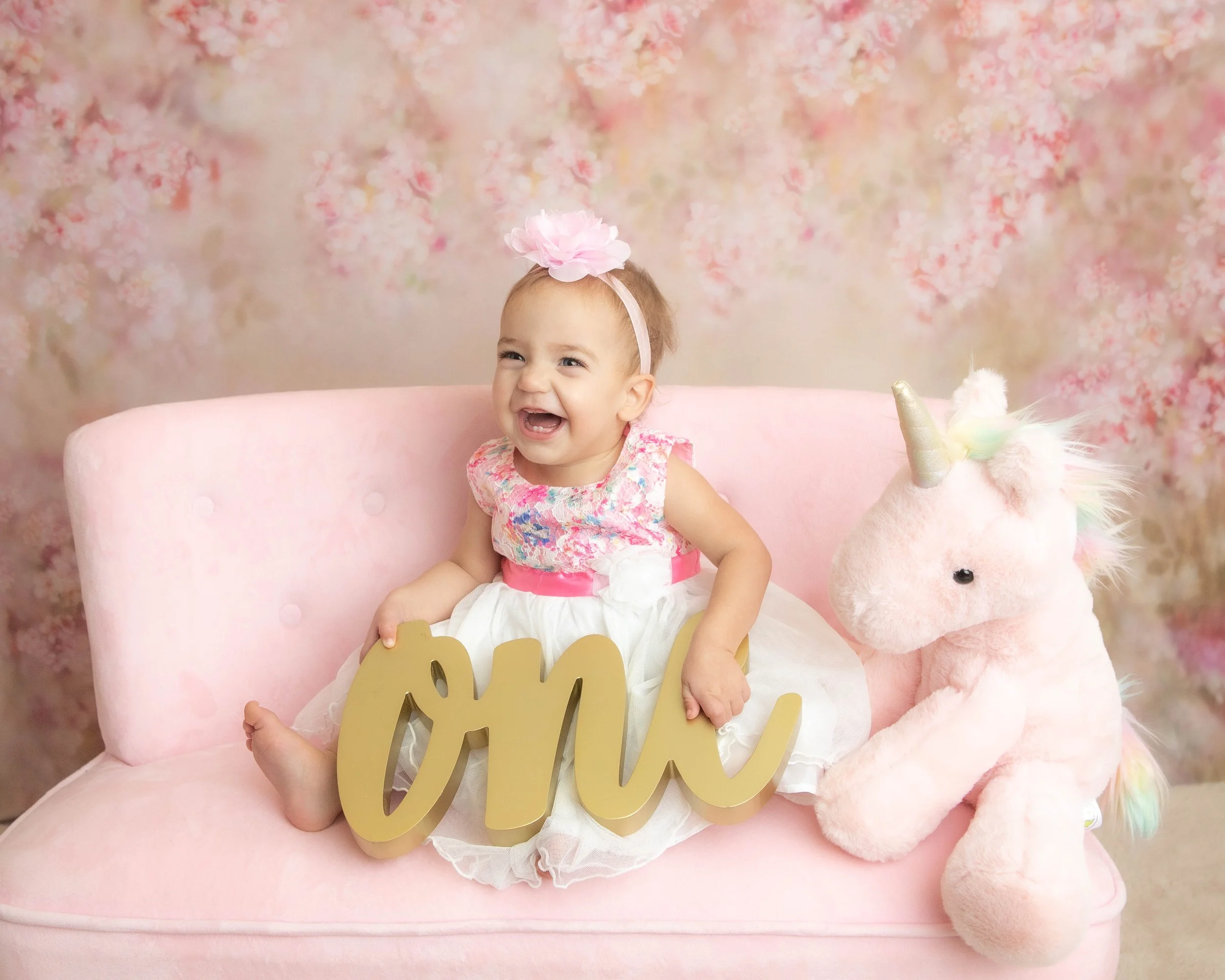 little girl sitting on pink sofa with the word ONE and a unicorn