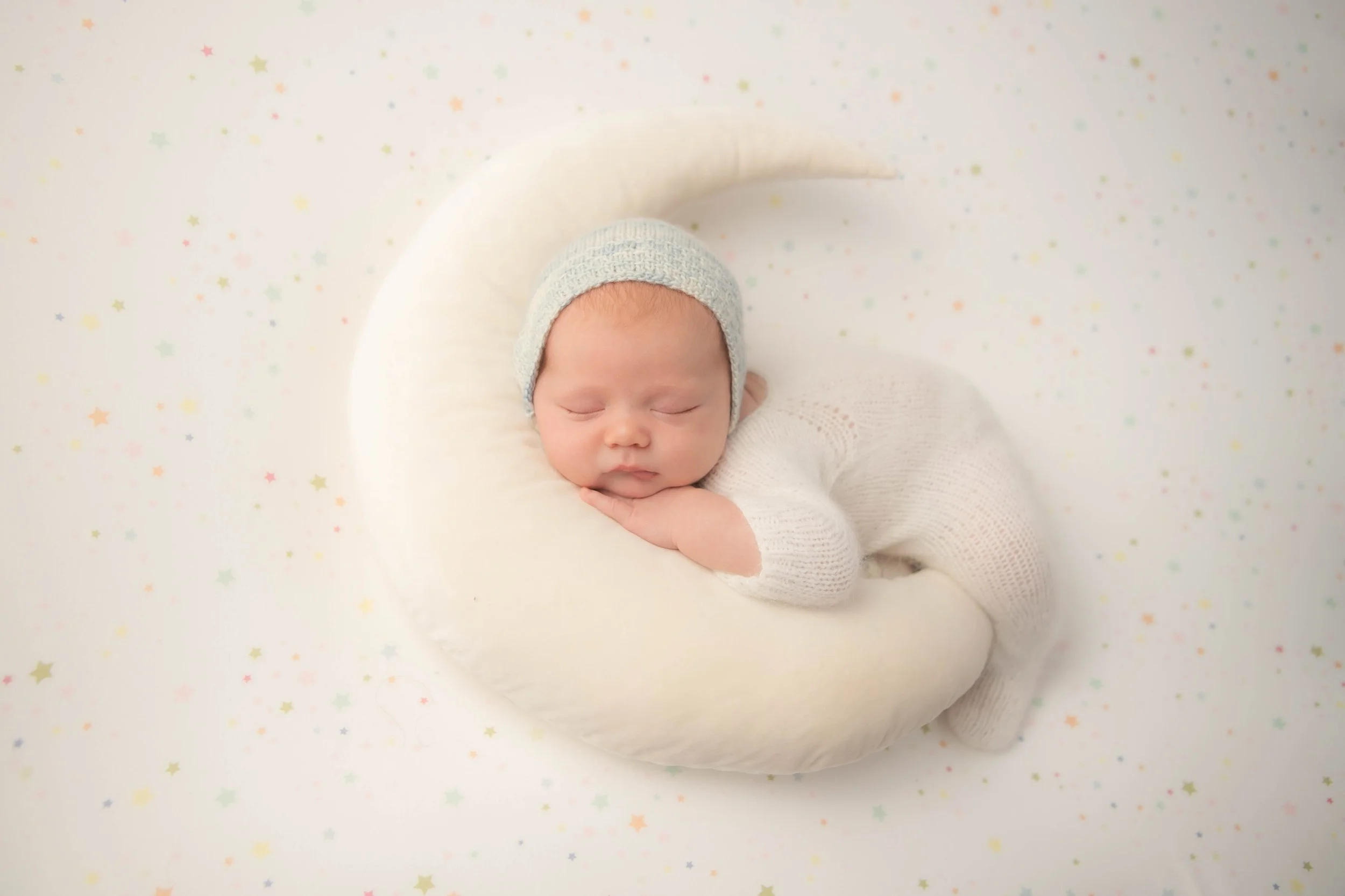 newbor baby boy dressed in white sleeping on a white moon
