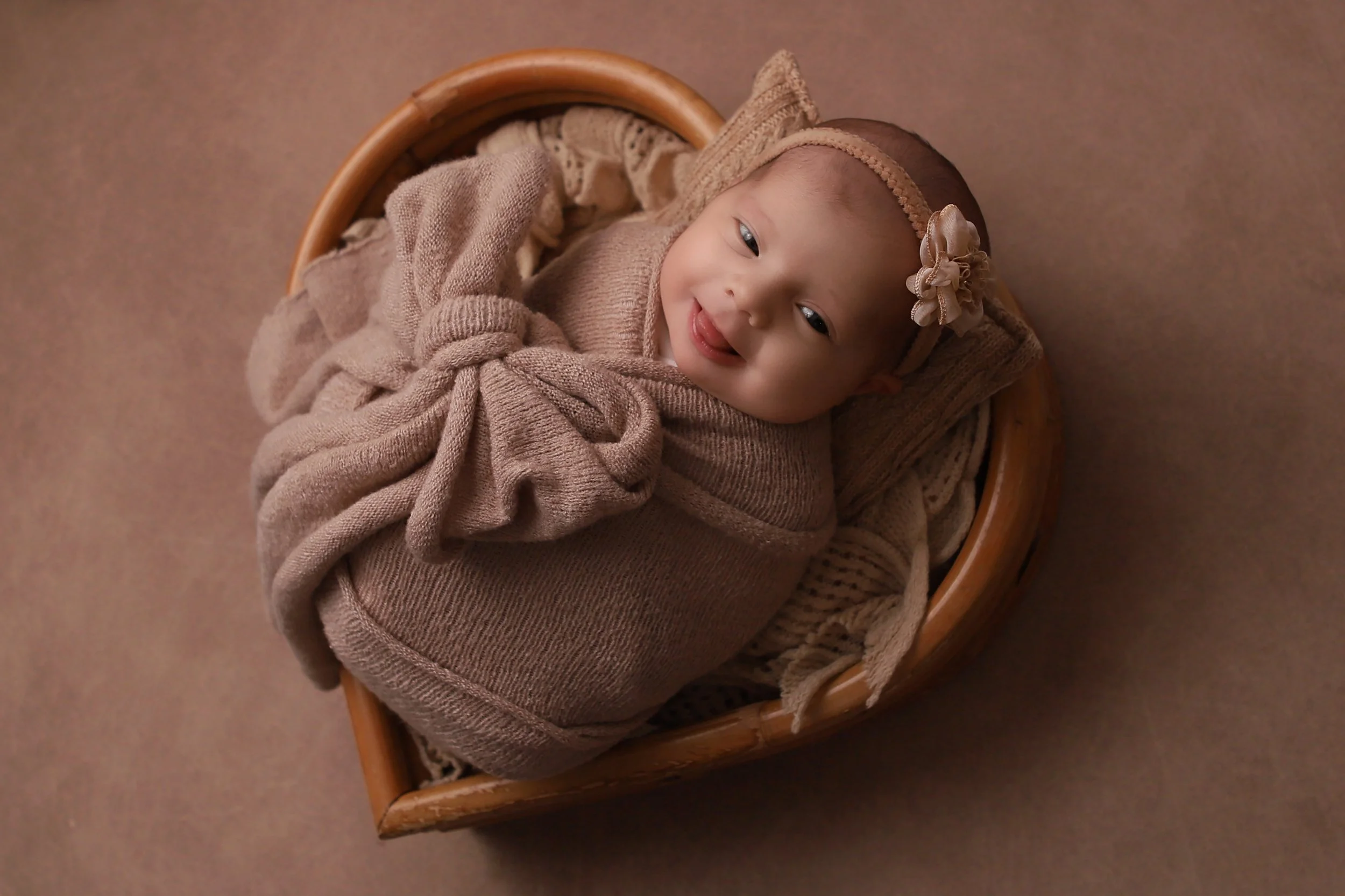 newborn baby girl wrapped in a beige swaddle with a bow