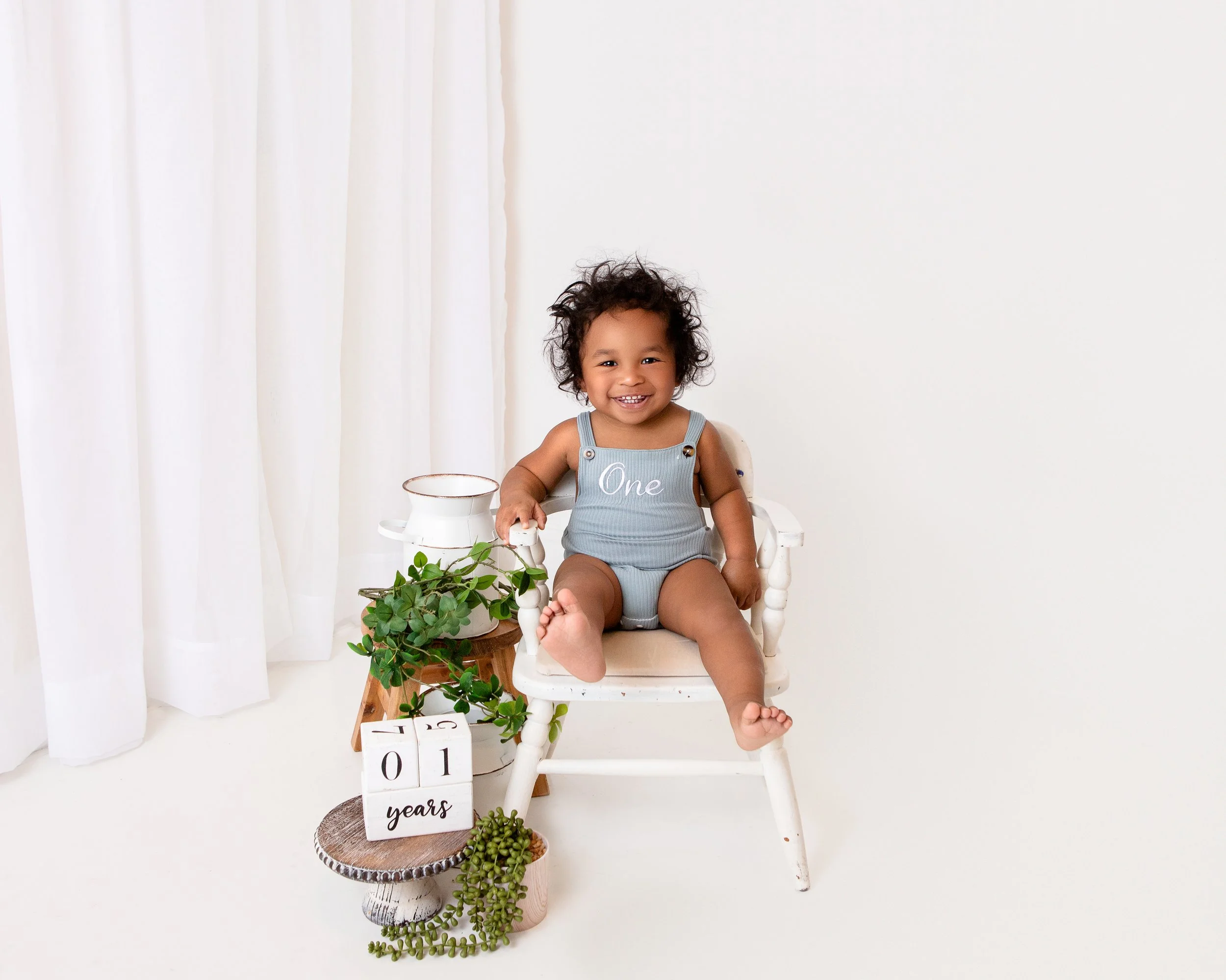one year old boy sitting in a chair with white walls and greenery