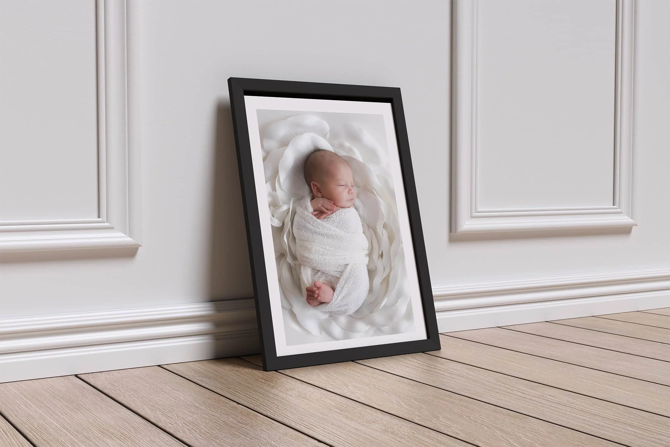 Framed newborn portrait leaning against a wall, showcasing a baby wrapped in white, nestled in a soft cloud-like blanket. Elegant and artistic newborn photography keepsake in Lancaster, PA.