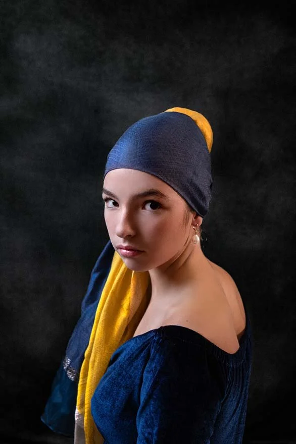 Girl with a pearl earring; Young woman wearing a blue and yellow headscarf, gazing intensely at the camera against a dark, moody backdrop. Artistic and dramatic fine art portrait photography in Lancaster, PA.
