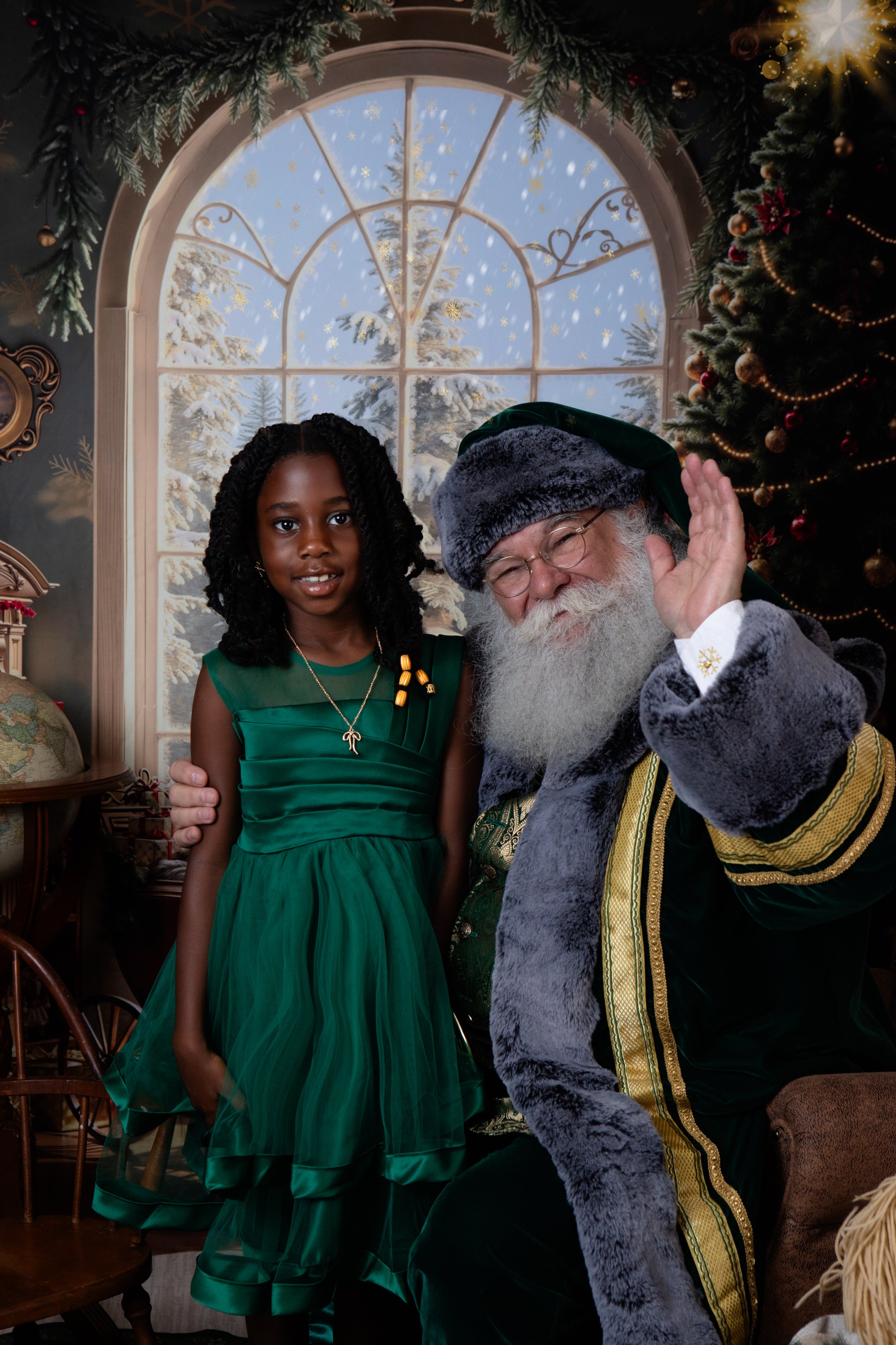 girl standing wearing a green dress lookingwhile Santa waves with a christmas windor scene behind them