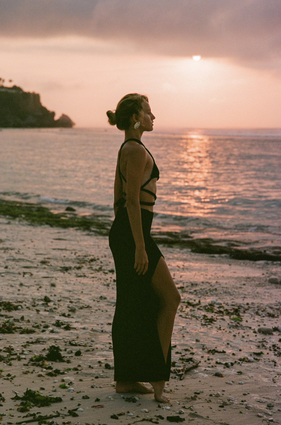 Woman in black dress standing on beach at sunset