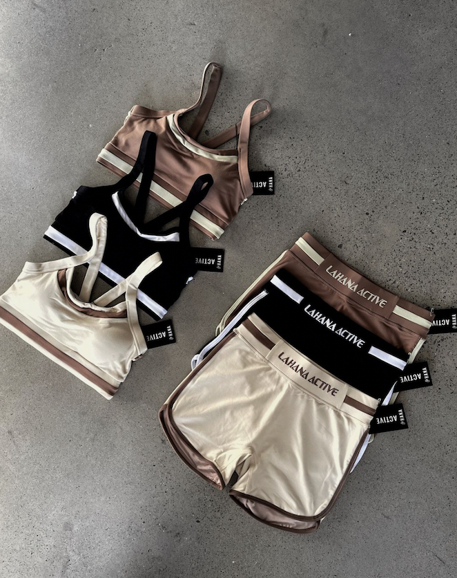 Athletic sets including sports bras and shorts in beige, black, and brown colors with 'Lahana Active' branding, displayed on a concrete floor.