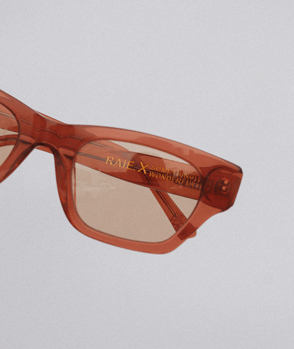 Close-up of orange-tinted glasses with "RAIE" and "SOMETHING WONDERFUL" text on the frame.