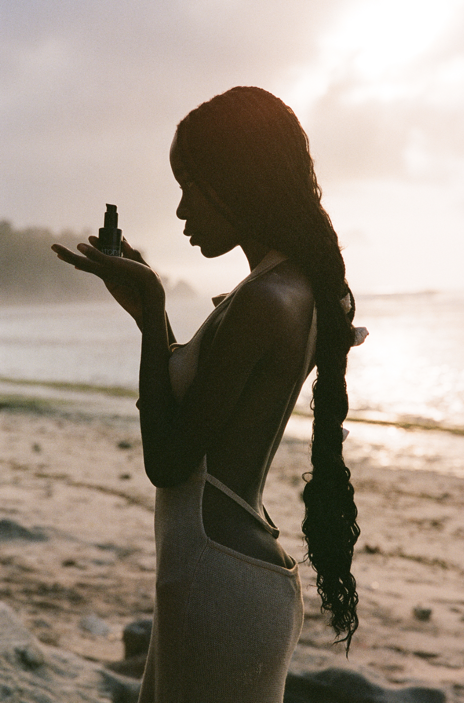 Silhouette of a woman holding a cosmetic bottle at the beach during sunset.