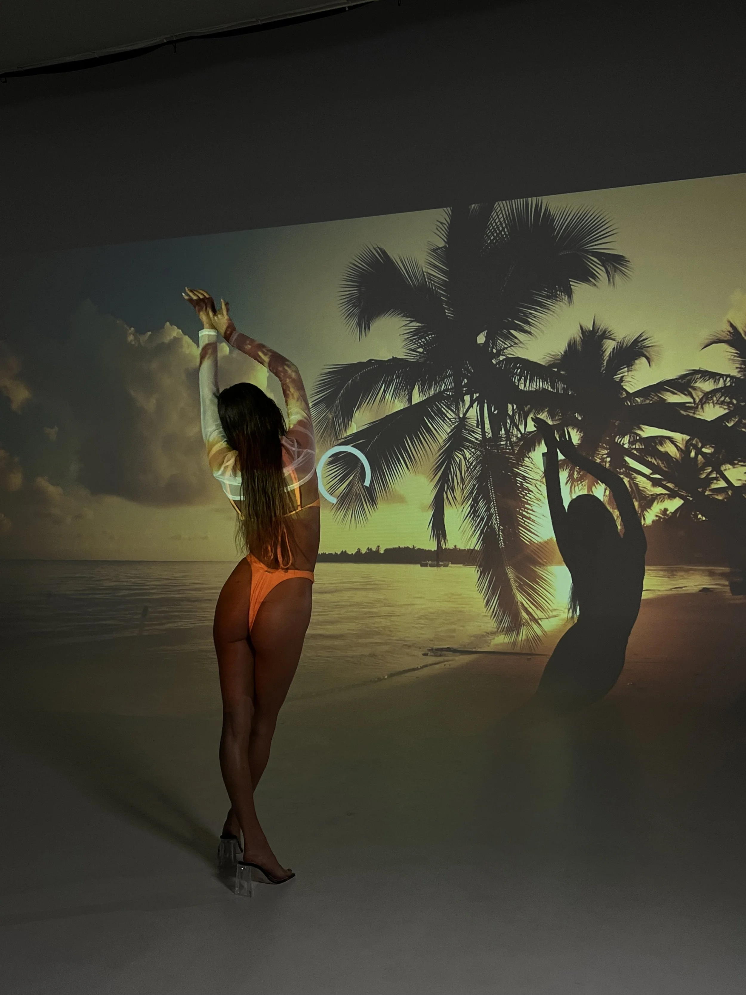 Person standing in front of a sunset beach projection with palm trees.