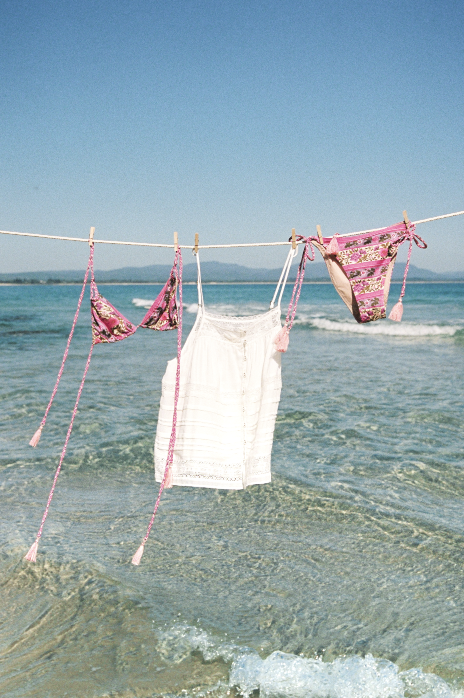Bikini and white dress hanging on a clothesline over the ocean.