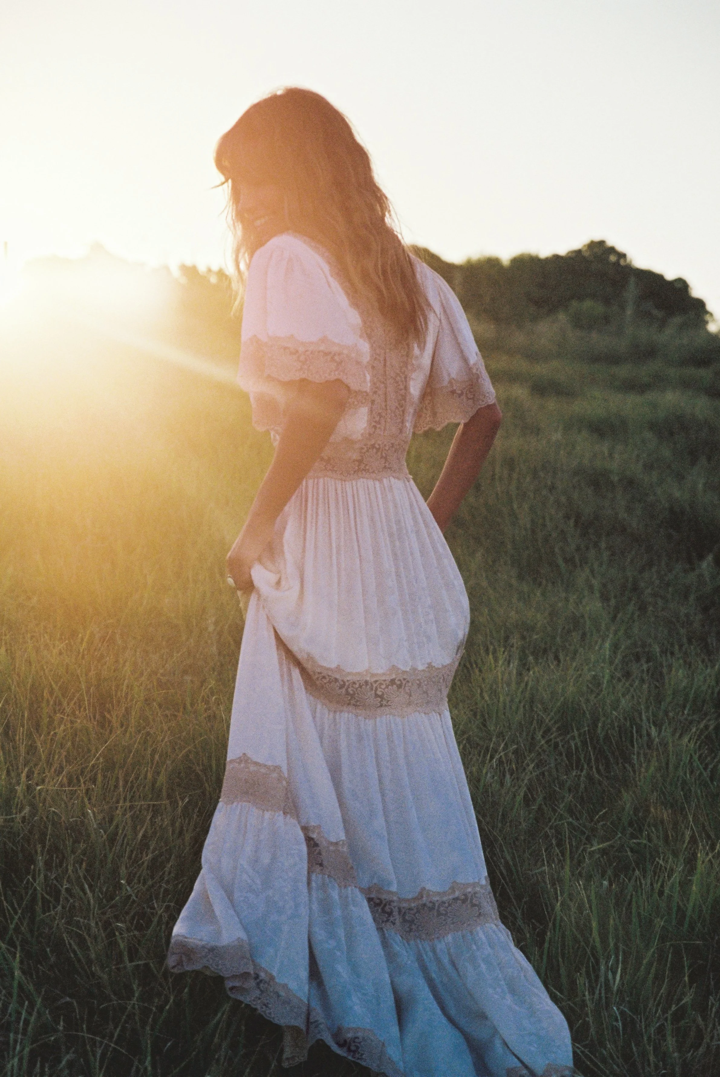 Woman in white dress walking in field at sunset