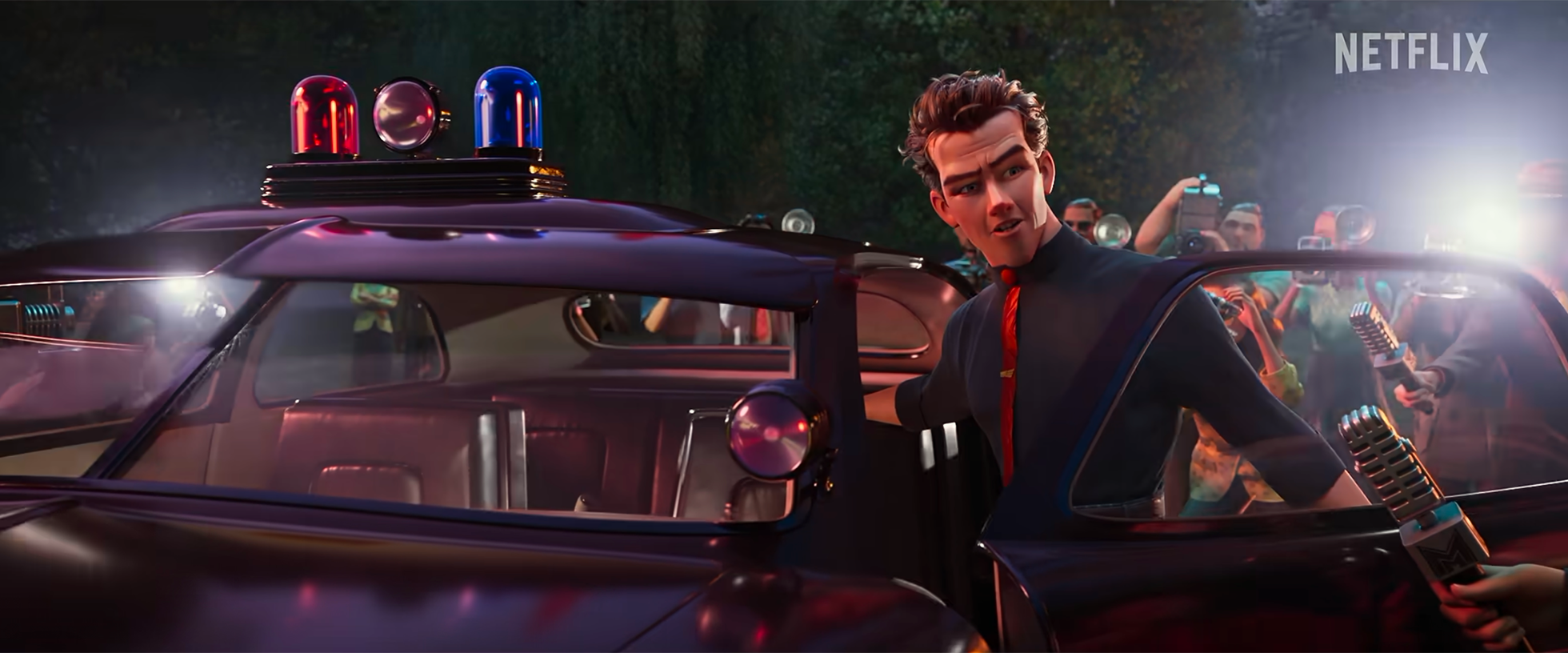 Animated scene featuring a man with dark curly hair dressed in a black shirt and red tie, standing next to a police car with emergency lights, surrounded by photographers and reporters with cameras and microphones, at night with trees in the backgrou