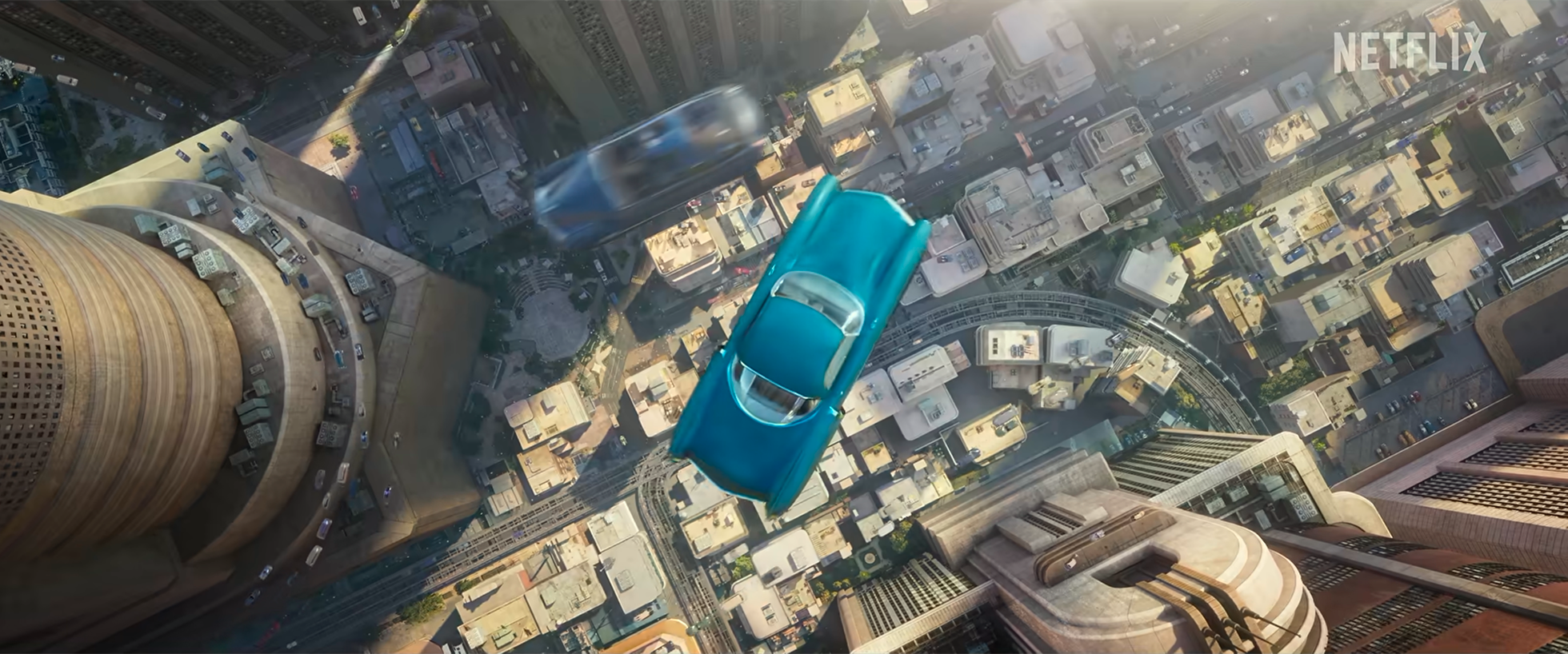 A blue car is falling off a building, with a cityscape of tall buildings and streets below. A blurred moving vehicle is also seen in the sky.