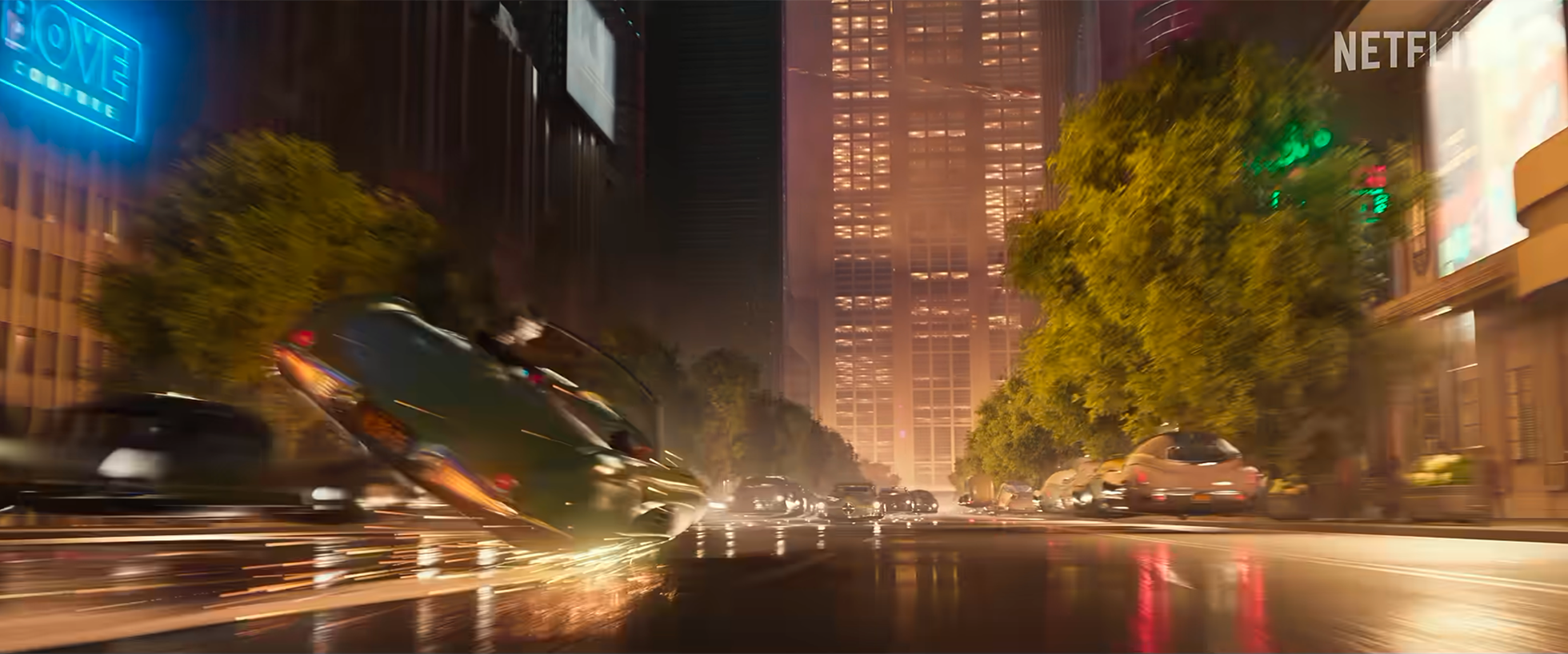 A city street at night with blurred cars and lights, tall buildings, and trees along the sidewalk.