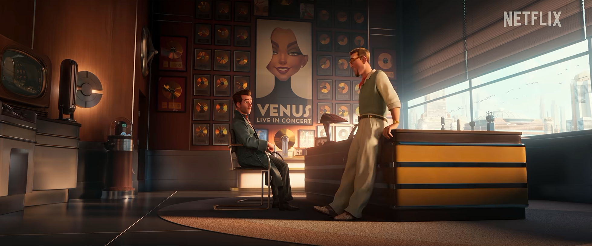 Animated scene of two men in an office. One man is sitting on a chair, the other is standing and leaning on a desk. The background features a wall decorated with framed gold records and a large poster of a woman labeled "Venus Live in Concert." Large