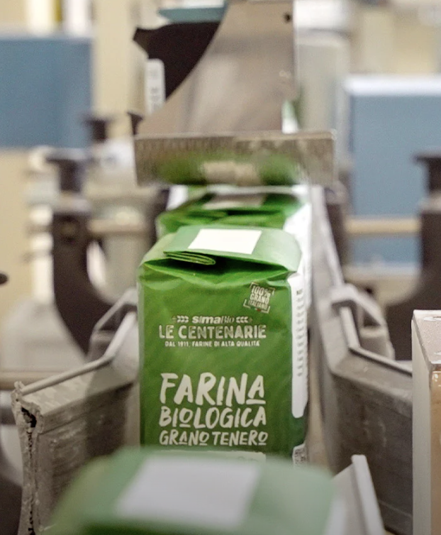 A green bag of organic wheat flour branded Molino Sima on a conveyor belt in a milling facility.