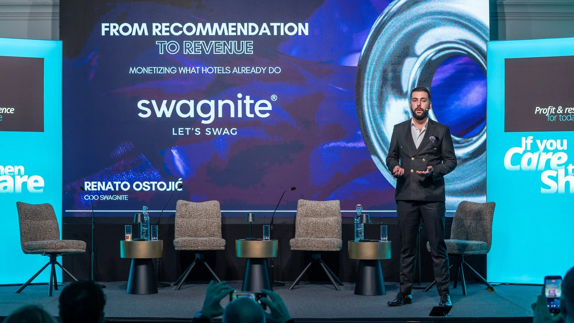 Man in a dark pinstripe suit giving a presentation on stage with a large digital screen behind him displaying the Swagnite logo and text about monetizing hotel services.
