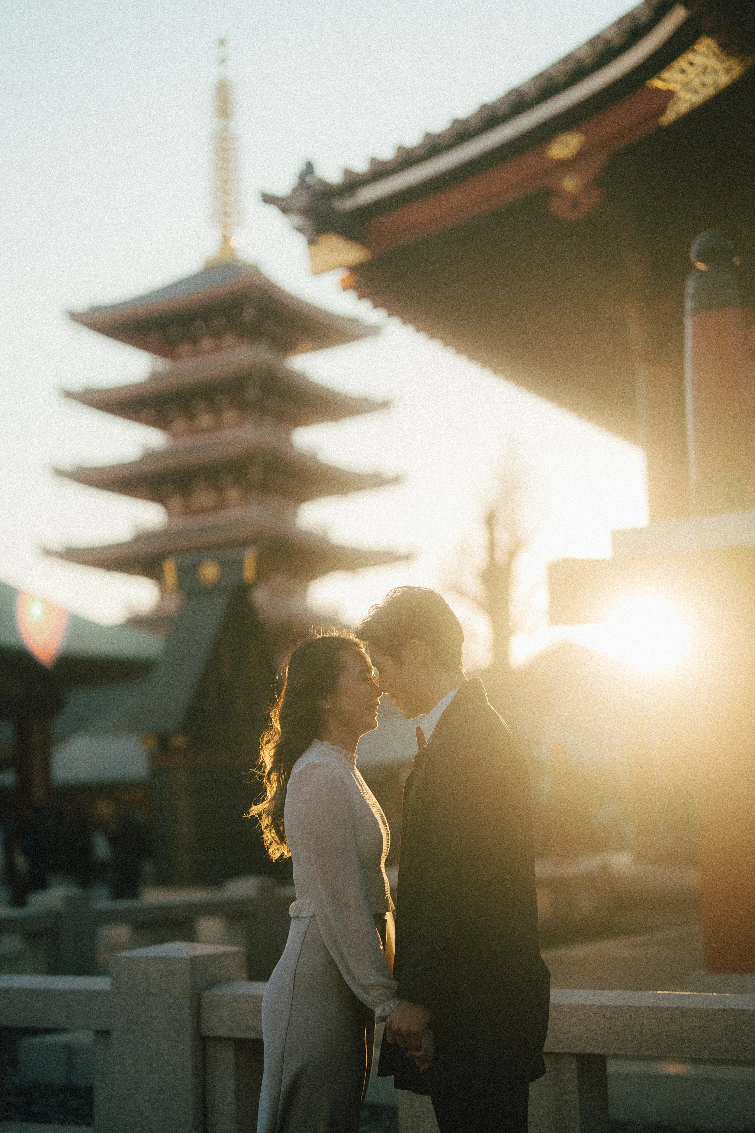 Couple posing for a photo with sunset light filtering through Sensoji Temple