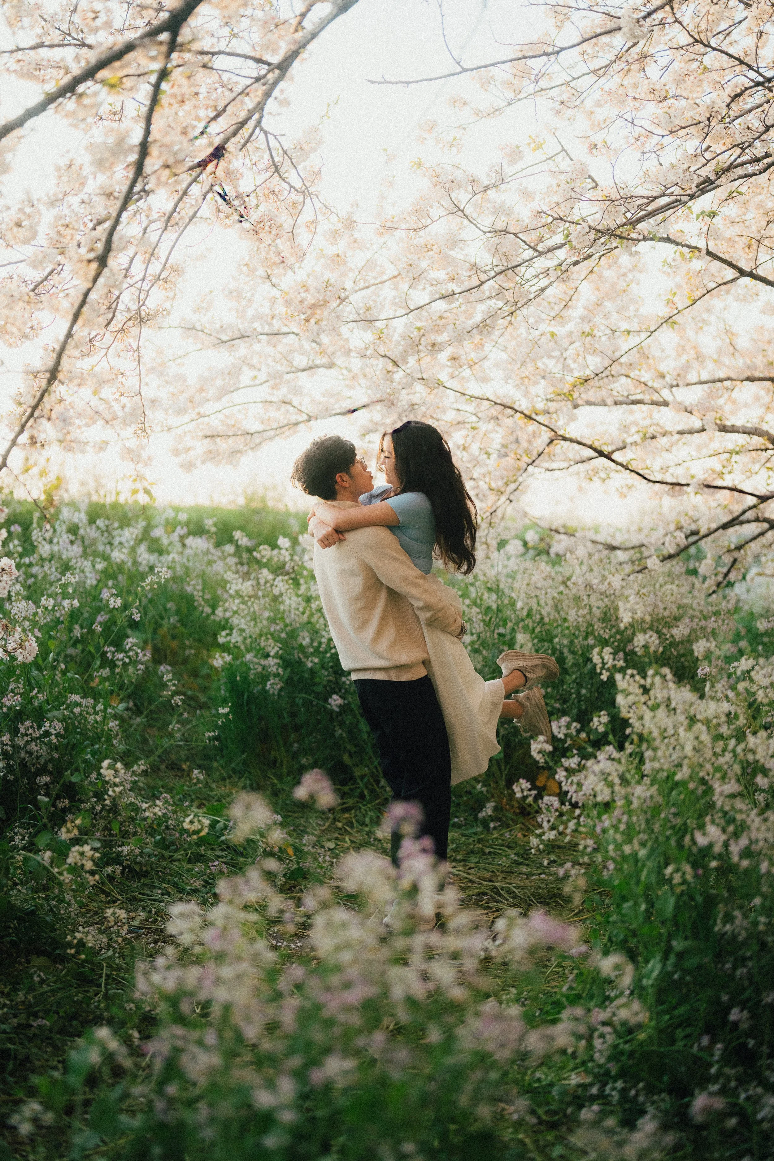 Man lifting his girlfriend off the ground, both surrounded by flowers - Tokyo couple photo session during the cherry blossom season