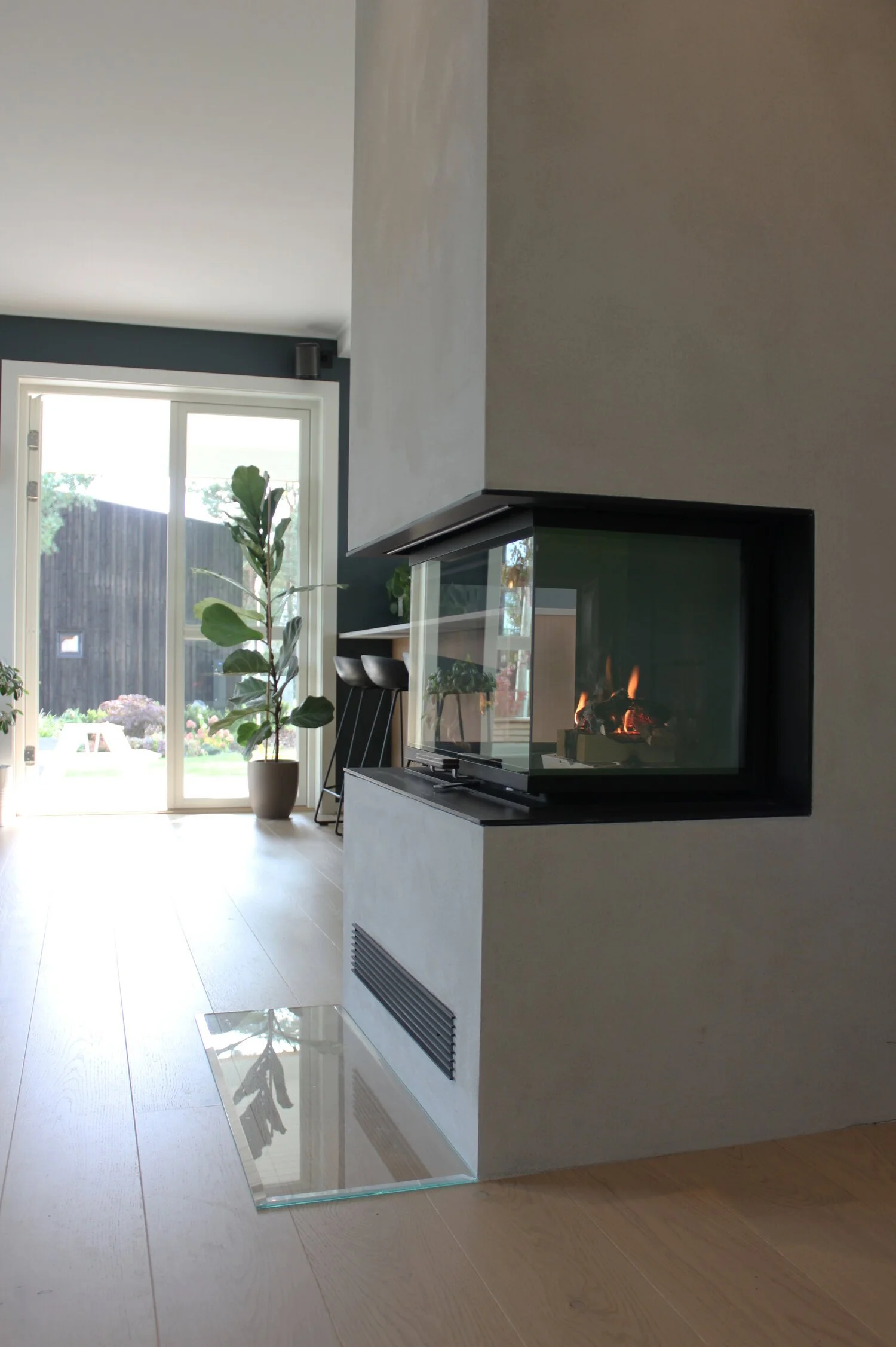 Det ble bygget peis med glass på tre sider som er synlig fra stue, spisestue og kjøkkenøy. Med peisinnsats og vednisje på den ene siden  og høyskap for oppbevaring på den andre siden, skapes en romdeler som gir den åpne løsningen intimitet. Se plansk