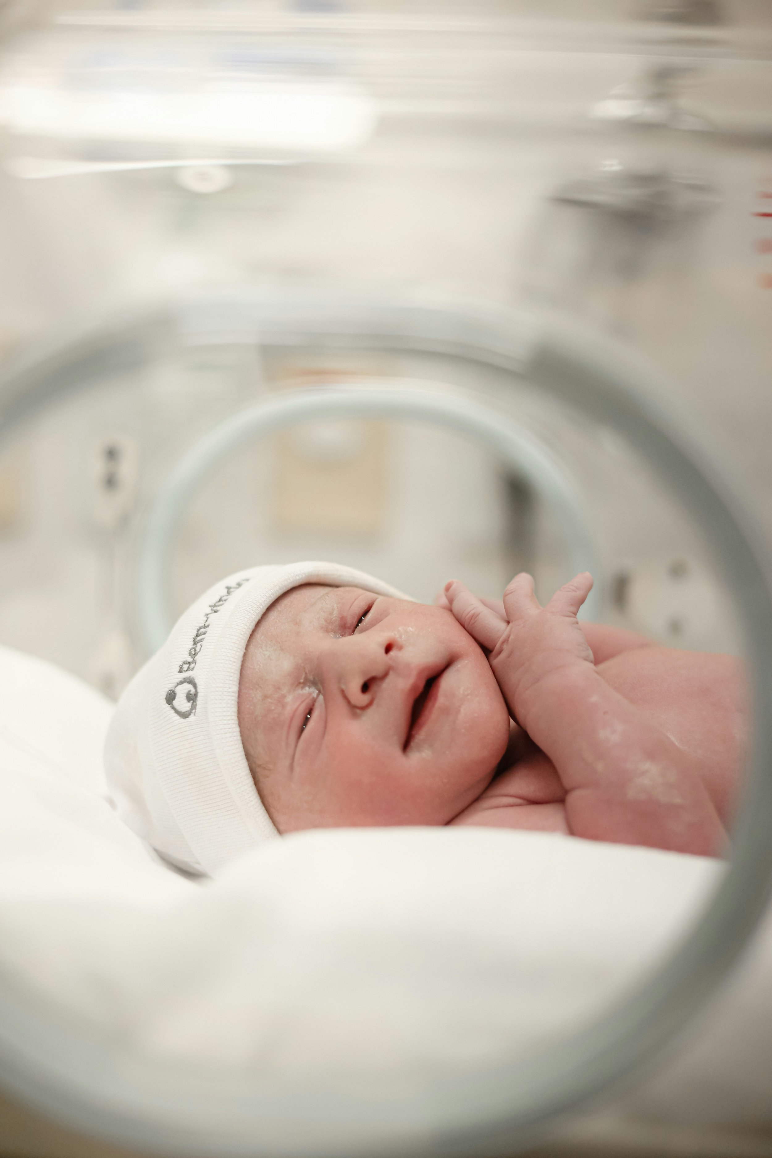 Newborn baby lay in NICU crib in white hat