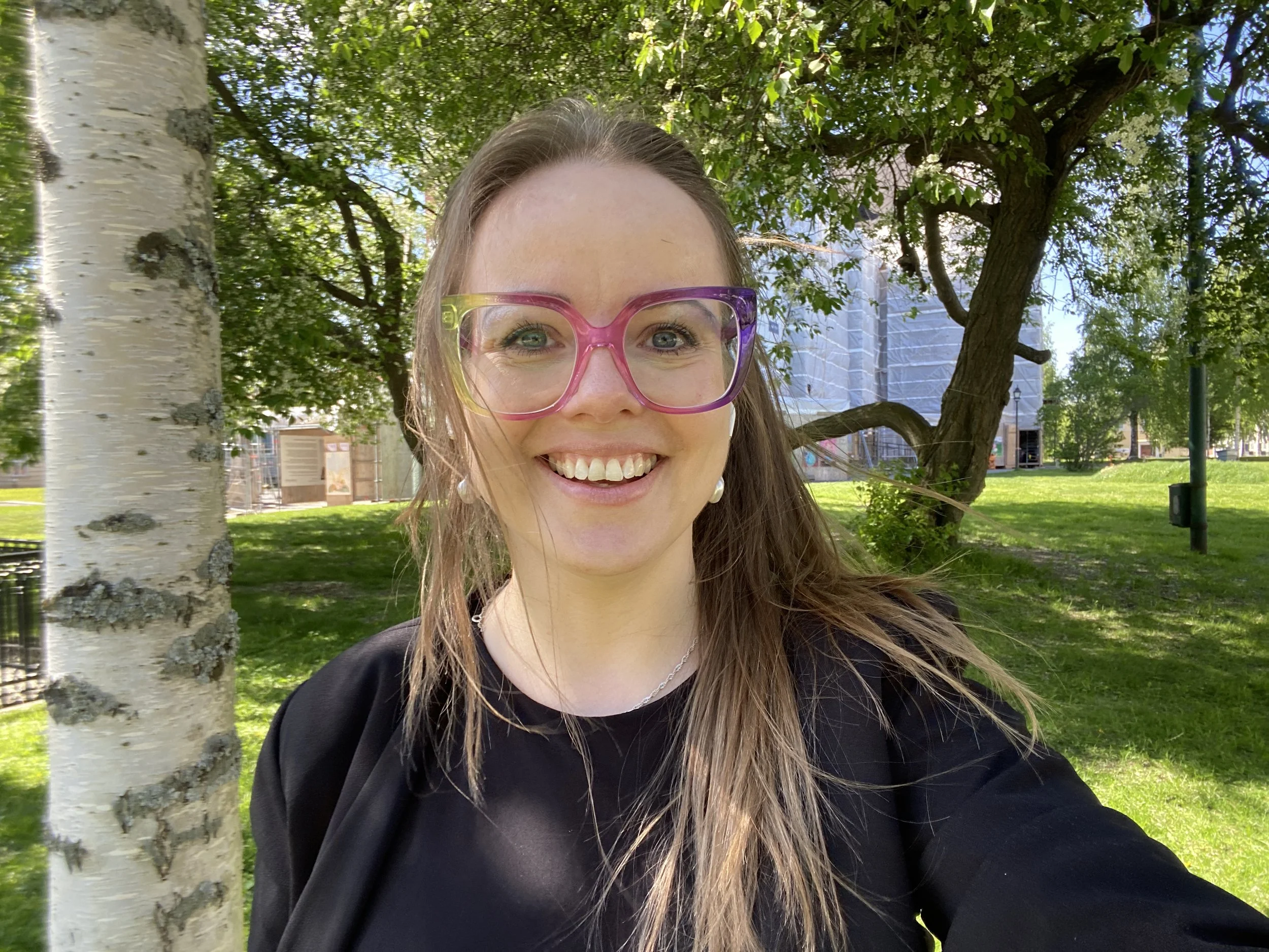 Welcome! Anna in nature with a big smile and colourful glasses.