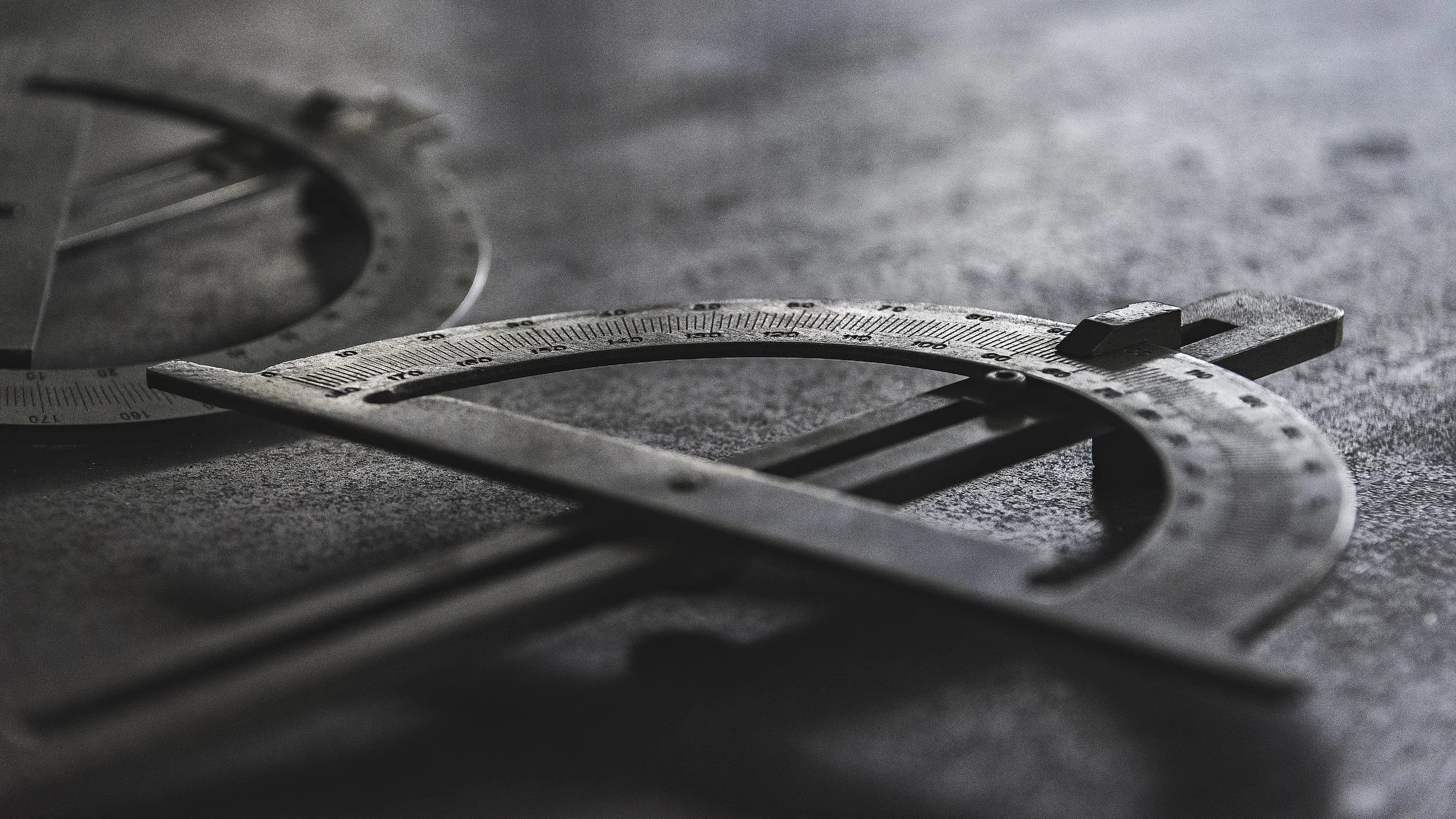 Close-up of a metal protractor and a steel ruler on a textured surface.