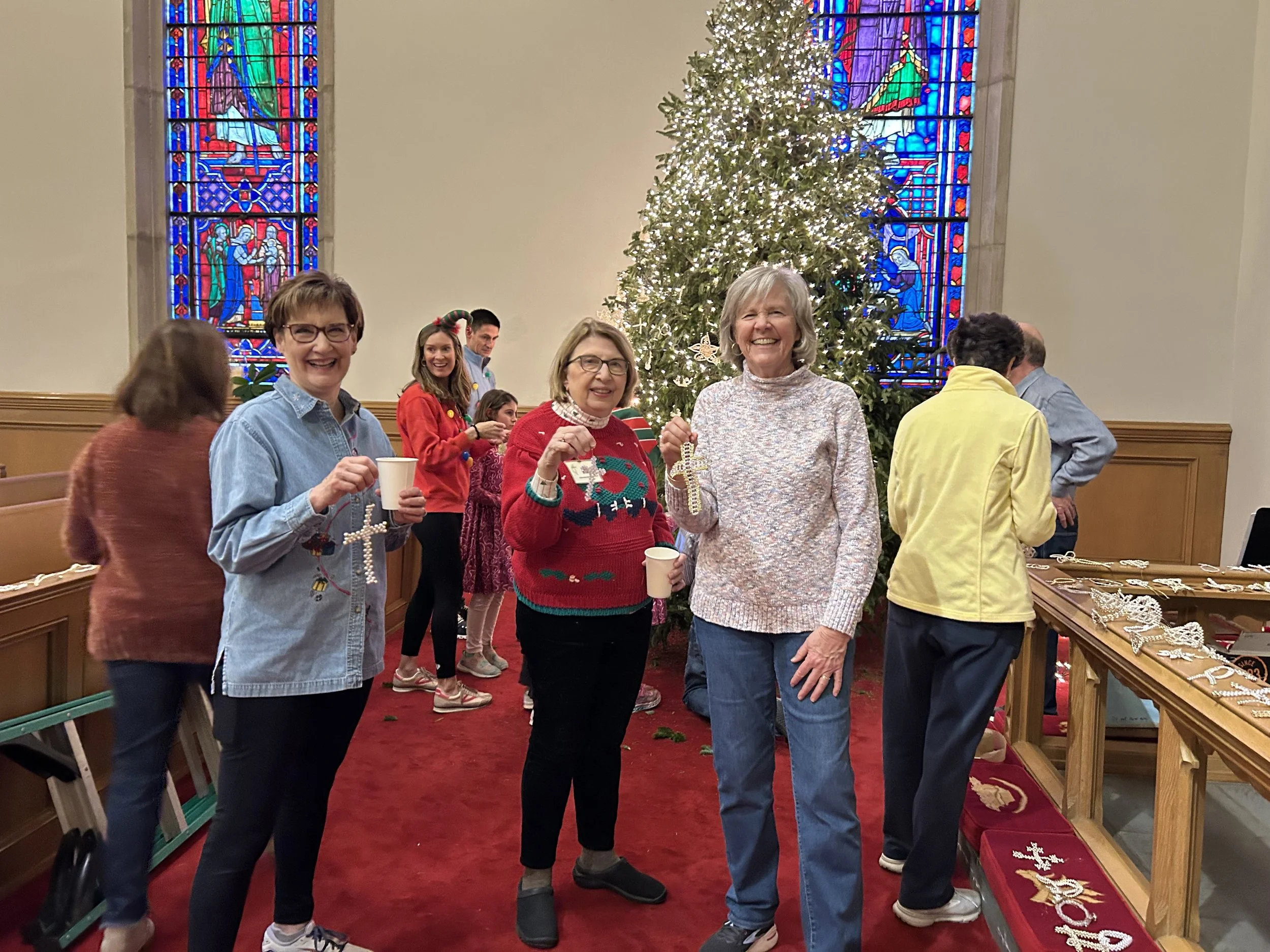People decorating a Christmas tree in a church with stained glass windows.