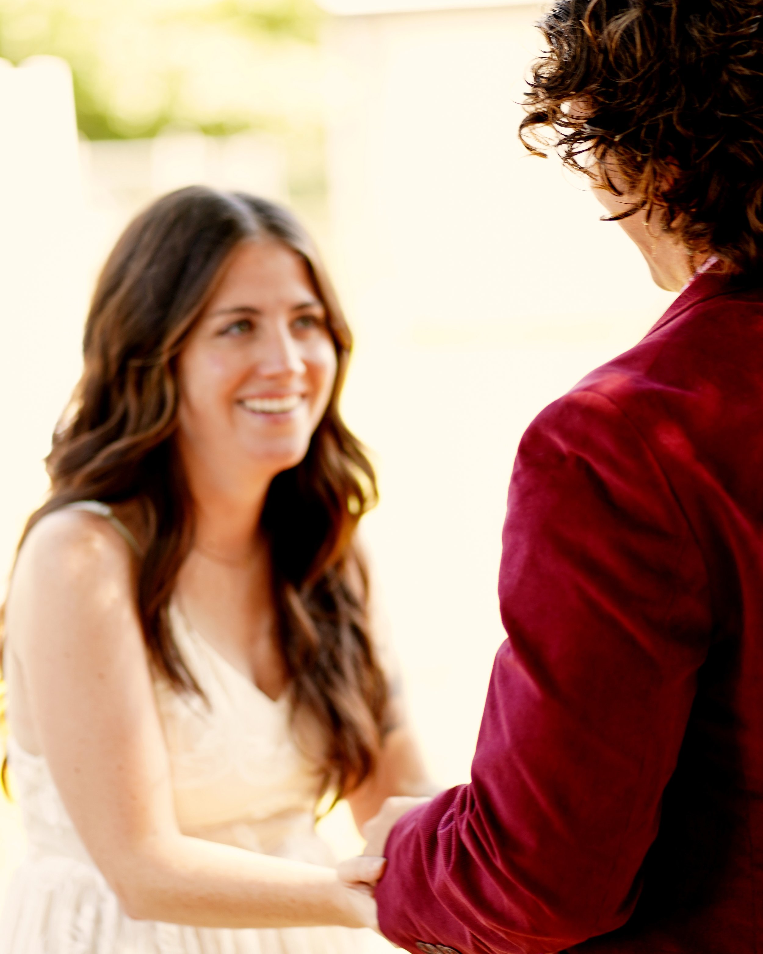 A smiling woman holding hands with a person in a red jacket outdoors.