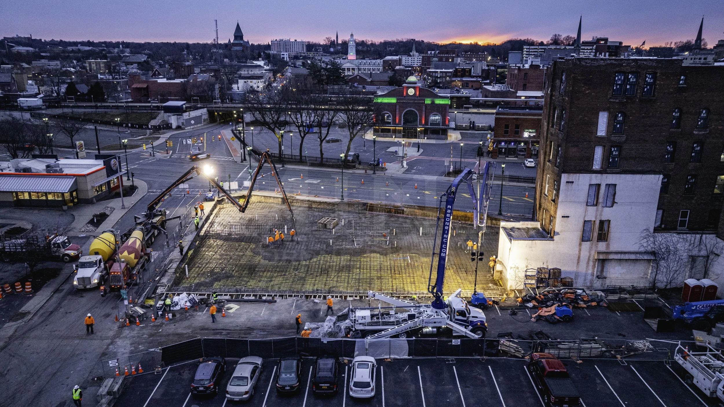 Construction site with workers and trucks at dusk in urban setting