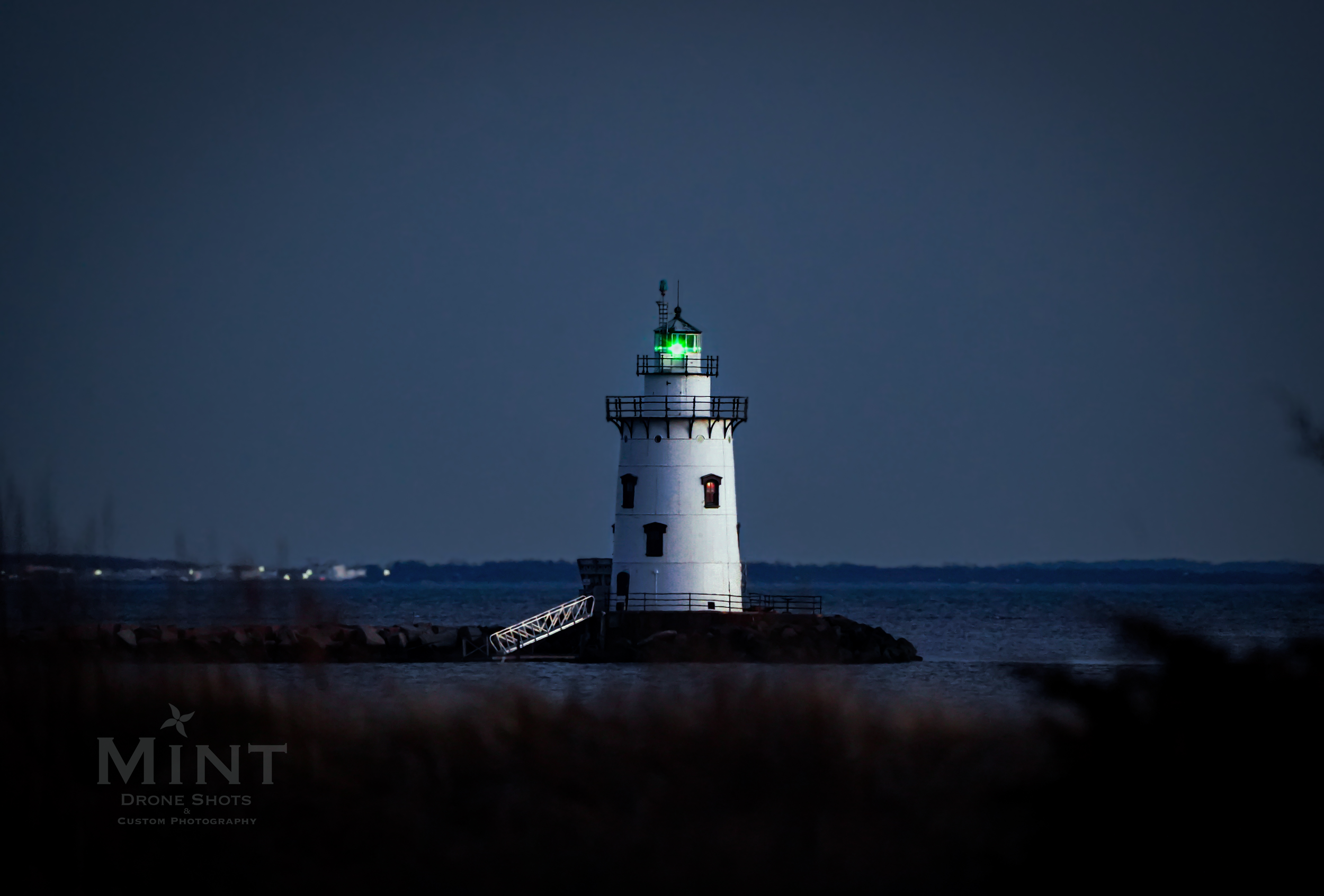 Lighthouse with a green light at night on a rocky shore.