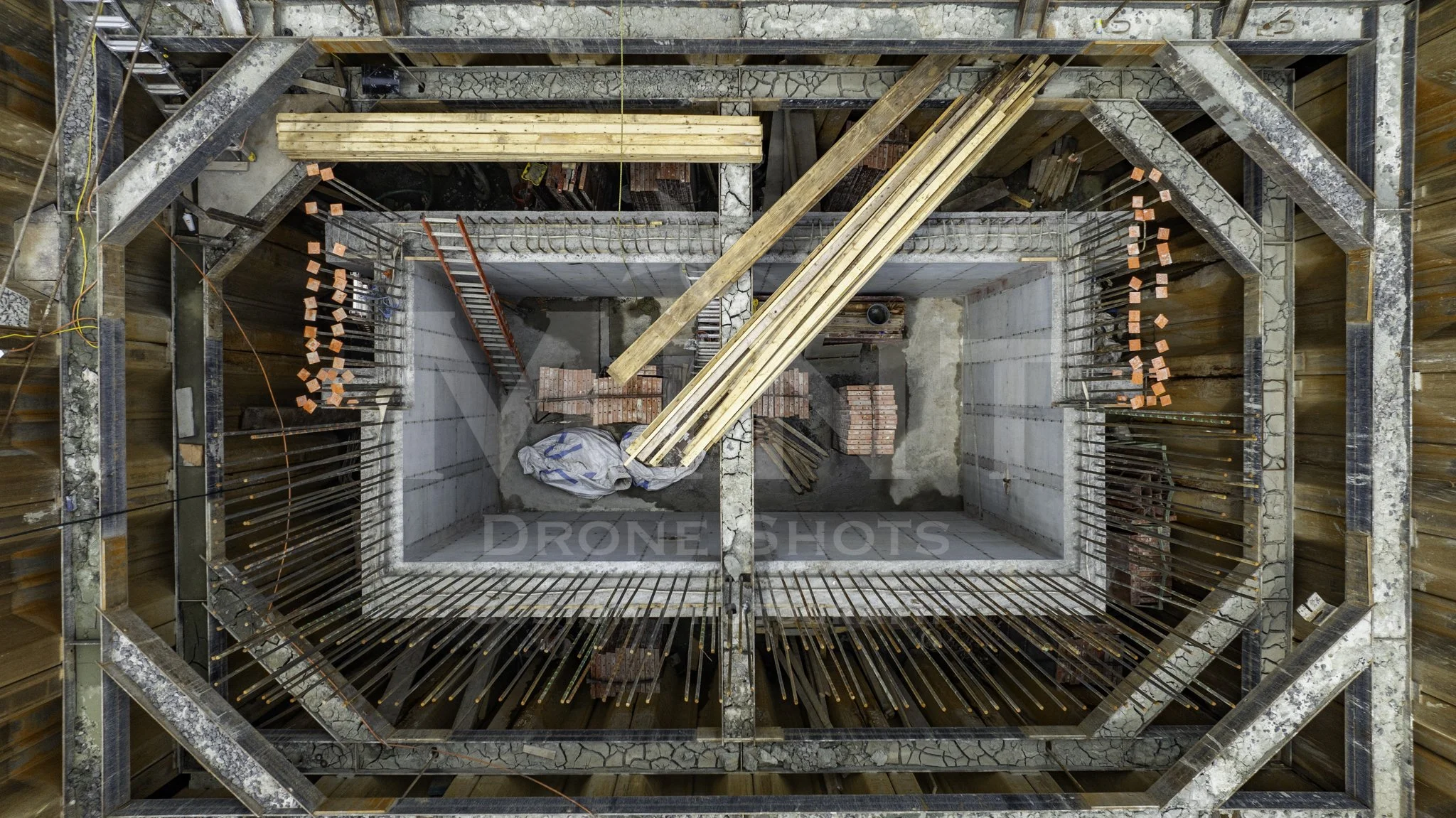 Aerial view of a construction site with wooden planks, steel reinforcement rods, bricks, and concrete forming a rectangular structure.
