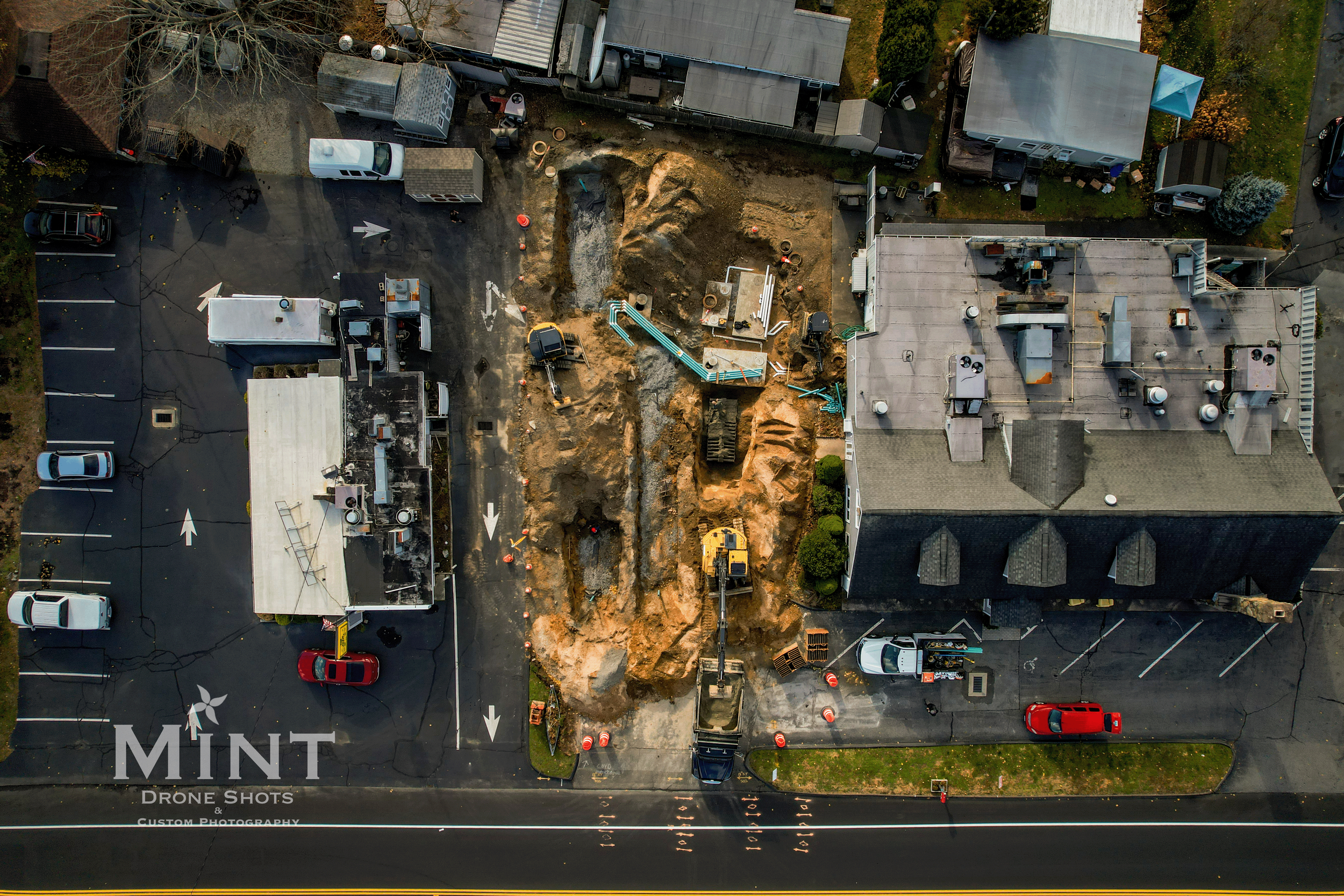 Aerial view of a construction site with heavy machinery between two buildings in a parking lot.