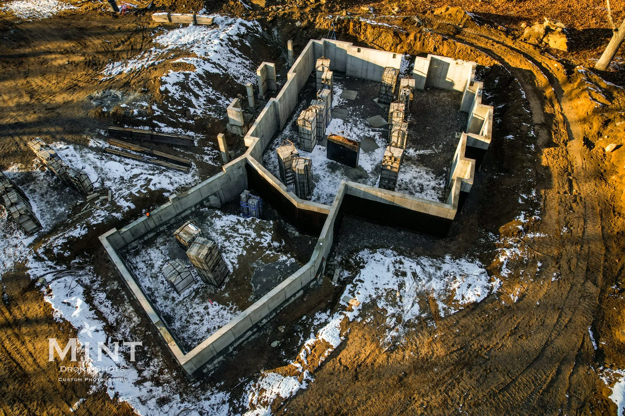 Aerial view of a building foundation under construction with snow on the ground.