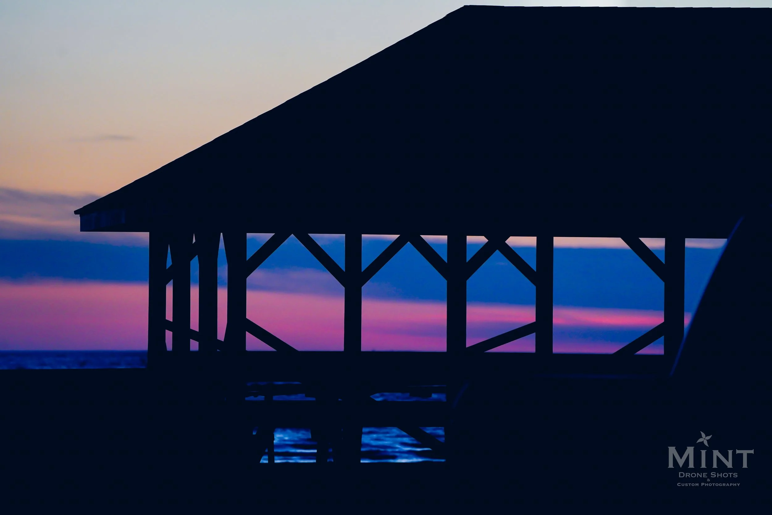 Silhouette of a beach gazebo at sunset with a purple and blue sky background.